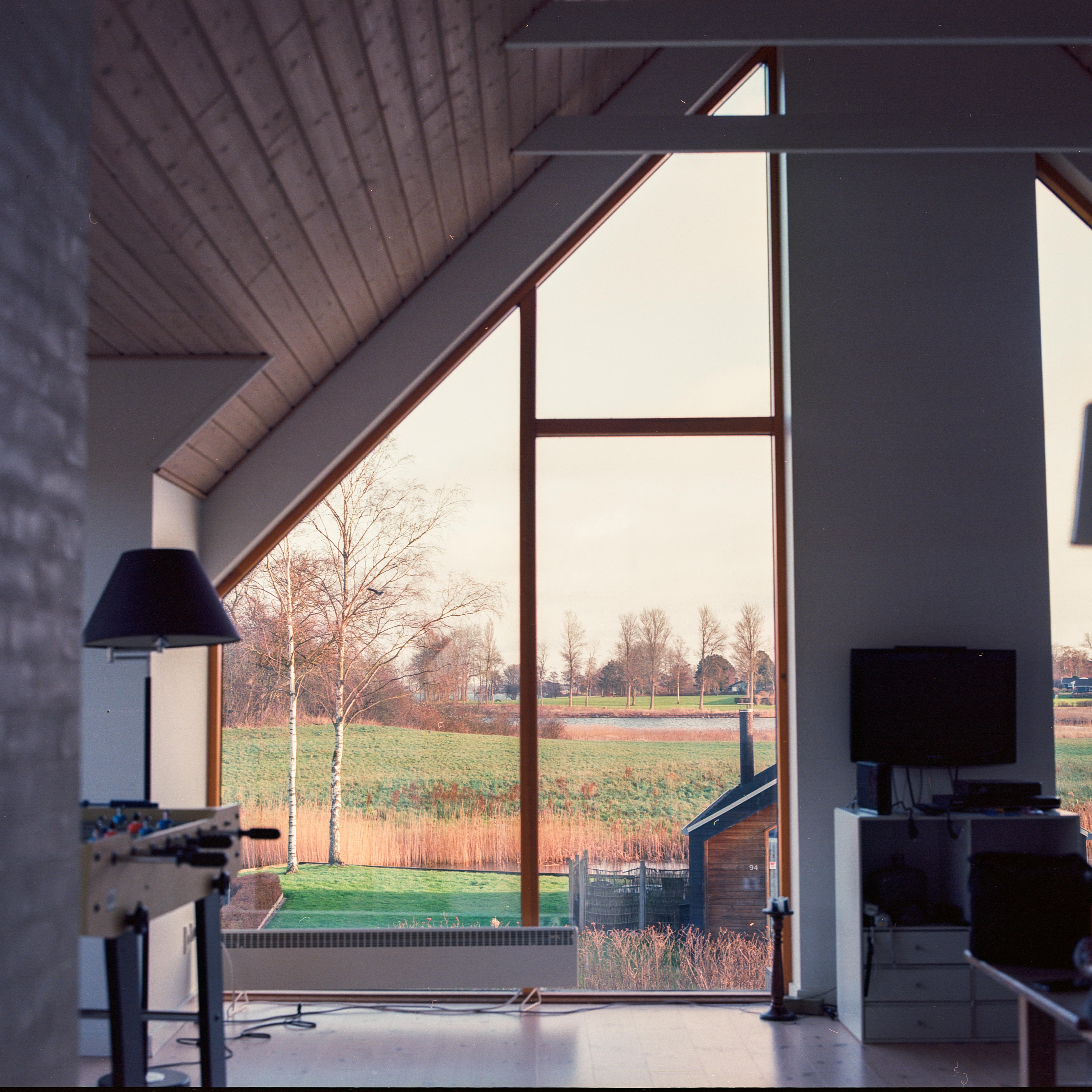 Opholdsrum i sommerhus med gulv til loft-vinduer og udsigt til åbent, grønt landskab og sø
