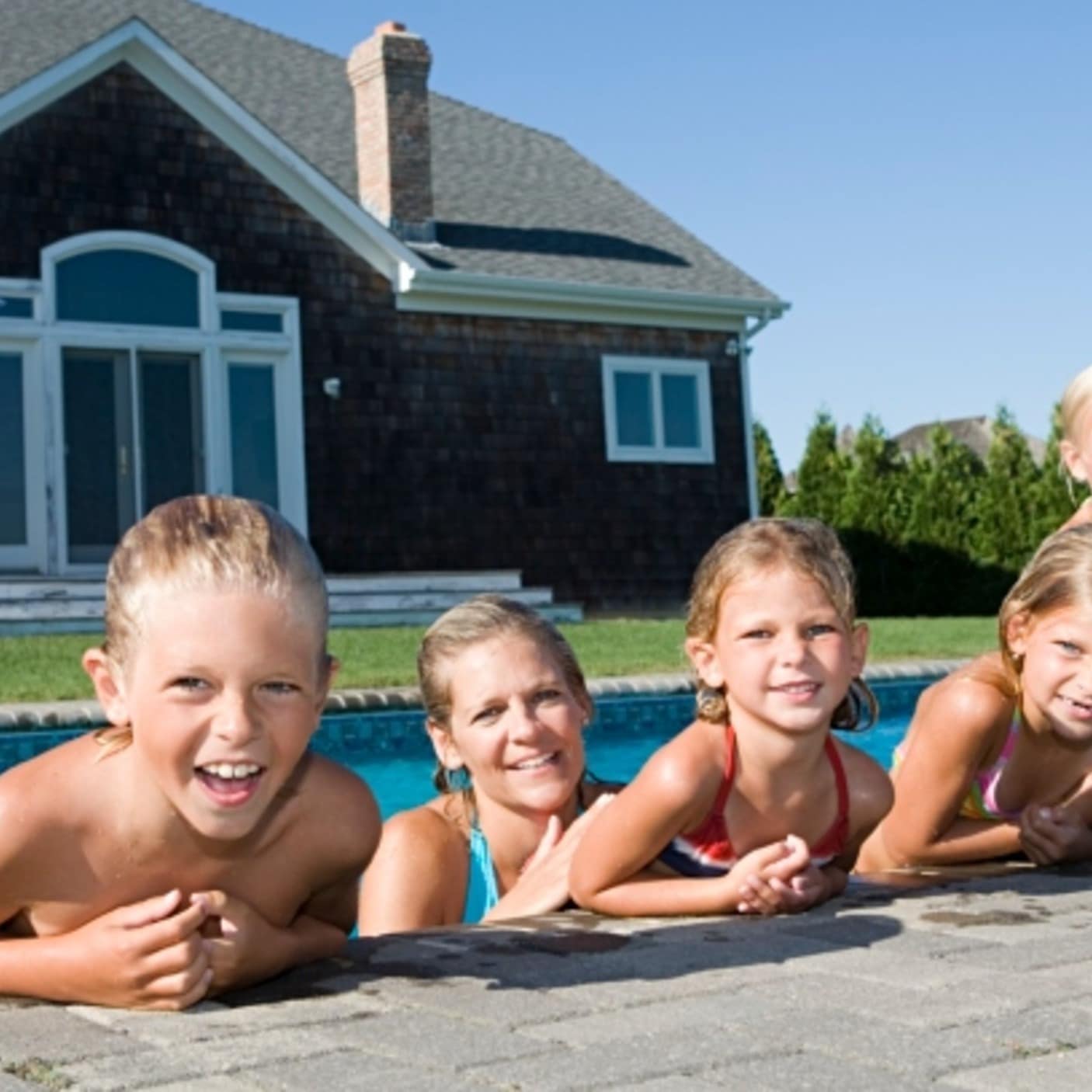 Familie ligger på kanten af en pool foran et sommerhus