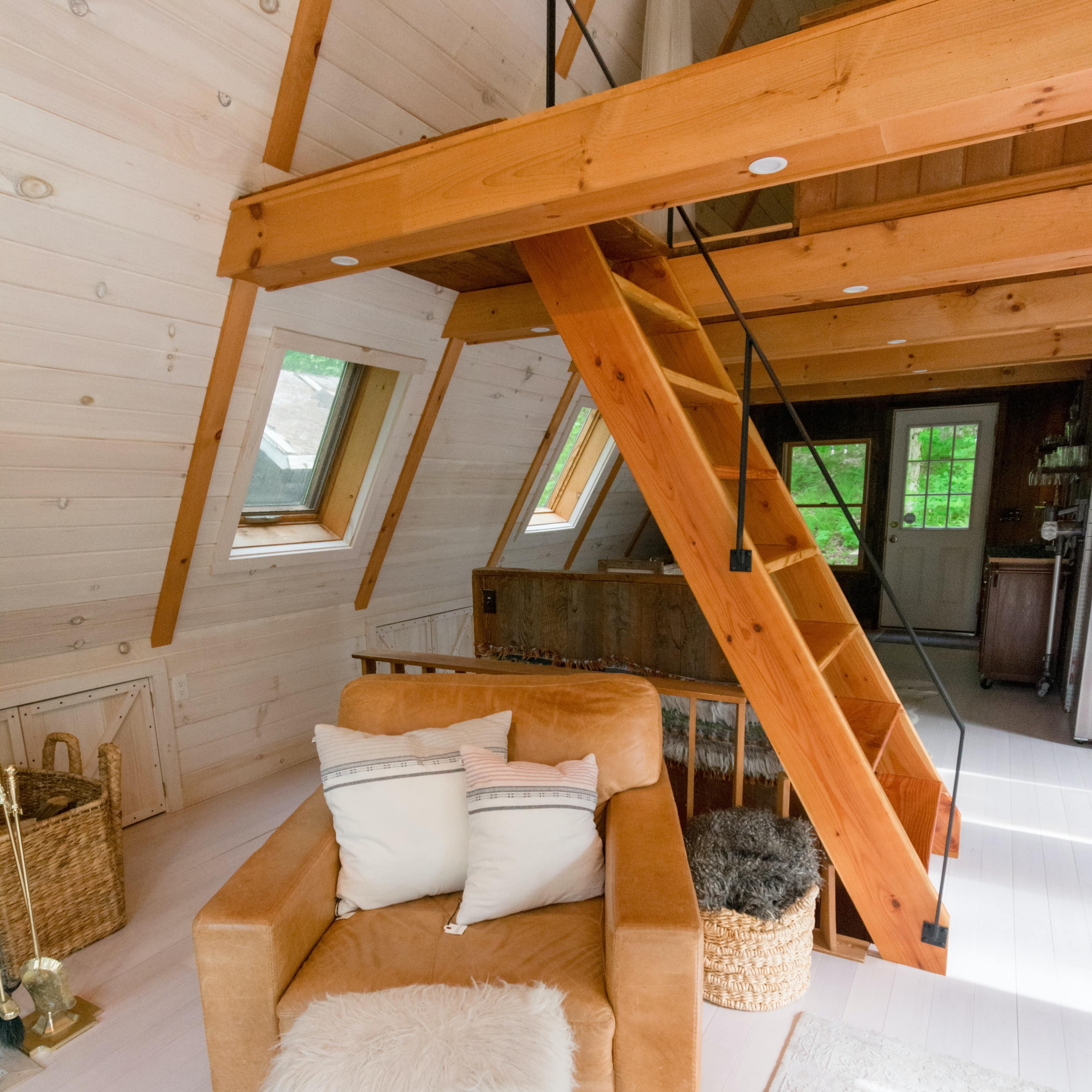 På billedet ses et hyggeligt sommerhus med skrå trævægge, en lænestol i forgrunden og en trappe op til hemsen.