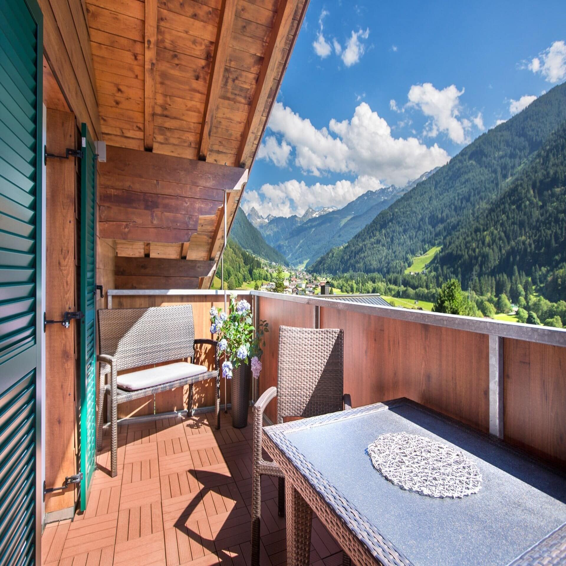 Holzbalkon mit Tisch und Sitzgelegenheiten und Blick auf das waldige und bergige Umland.