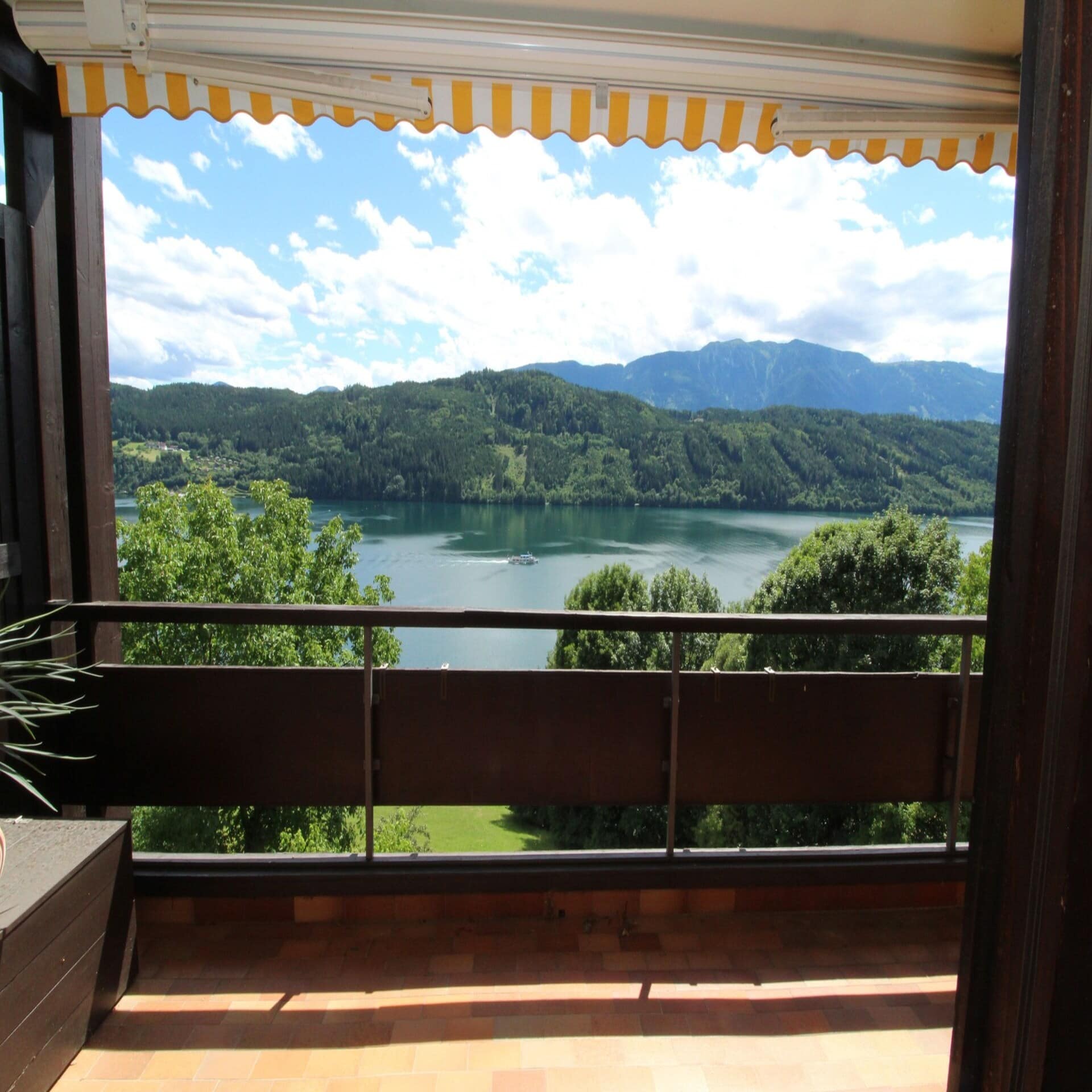 Balkon mit gelb-weiß gestreifter Markise direkt am See.