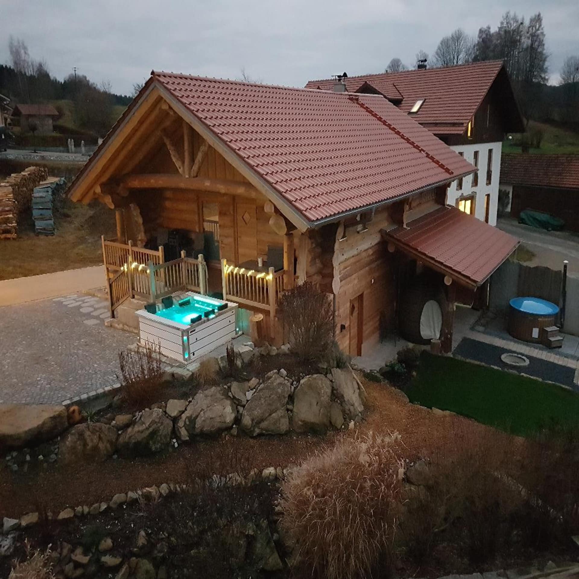 Ein Blockhaus mit beleuchtetem Whirlpool davor in der Abenddämmerung.