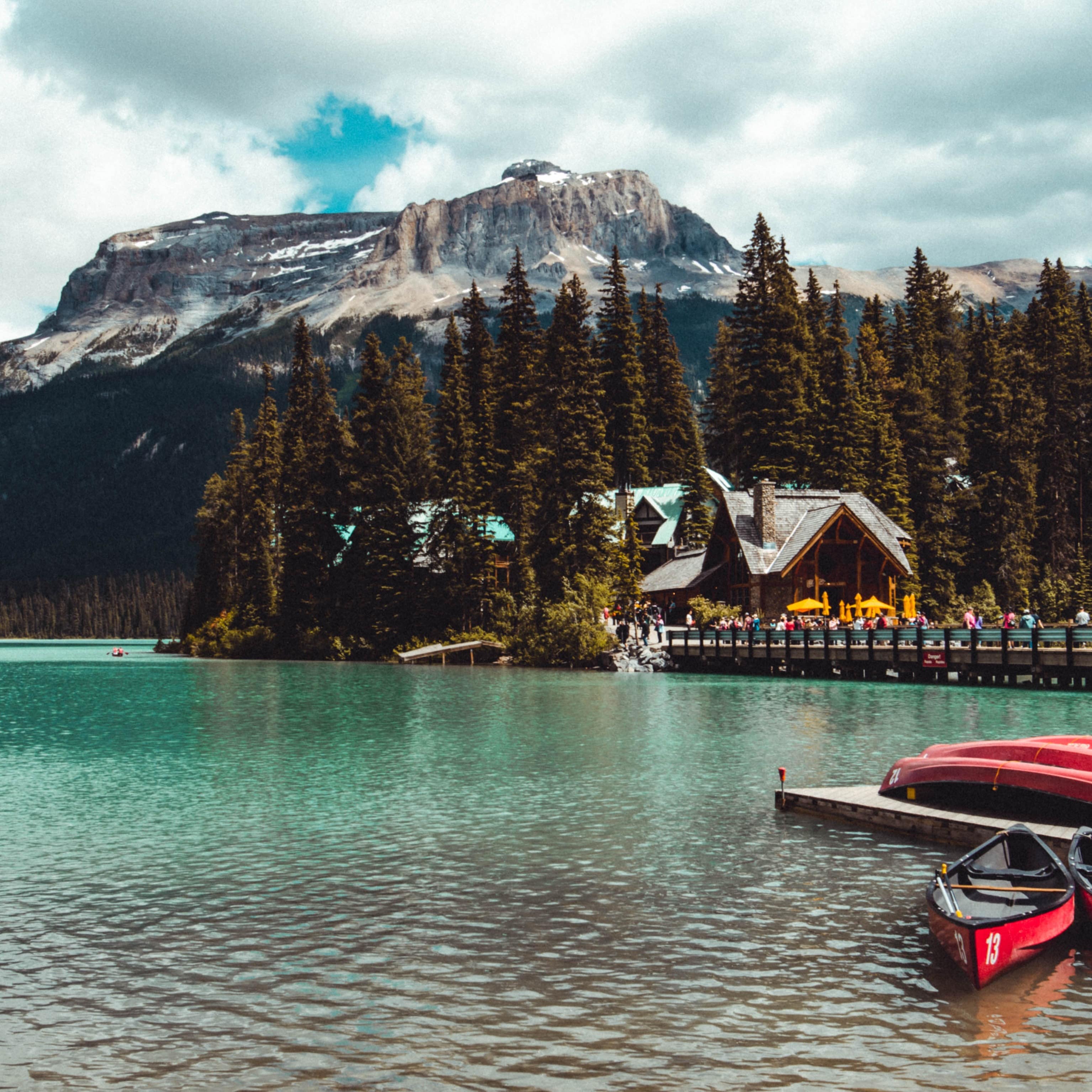 Red kayaks on a deck with a lodge across the water at Emerald Lake with mountains in the background