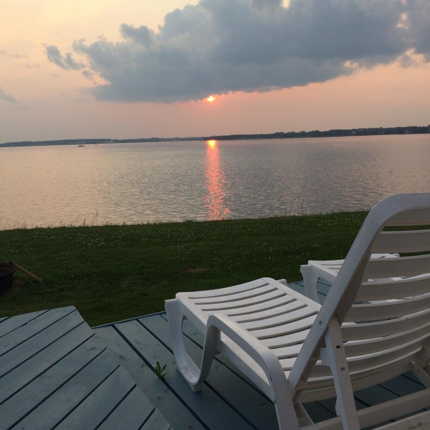 View of sunset over harbour from deck with white adirondack chairs