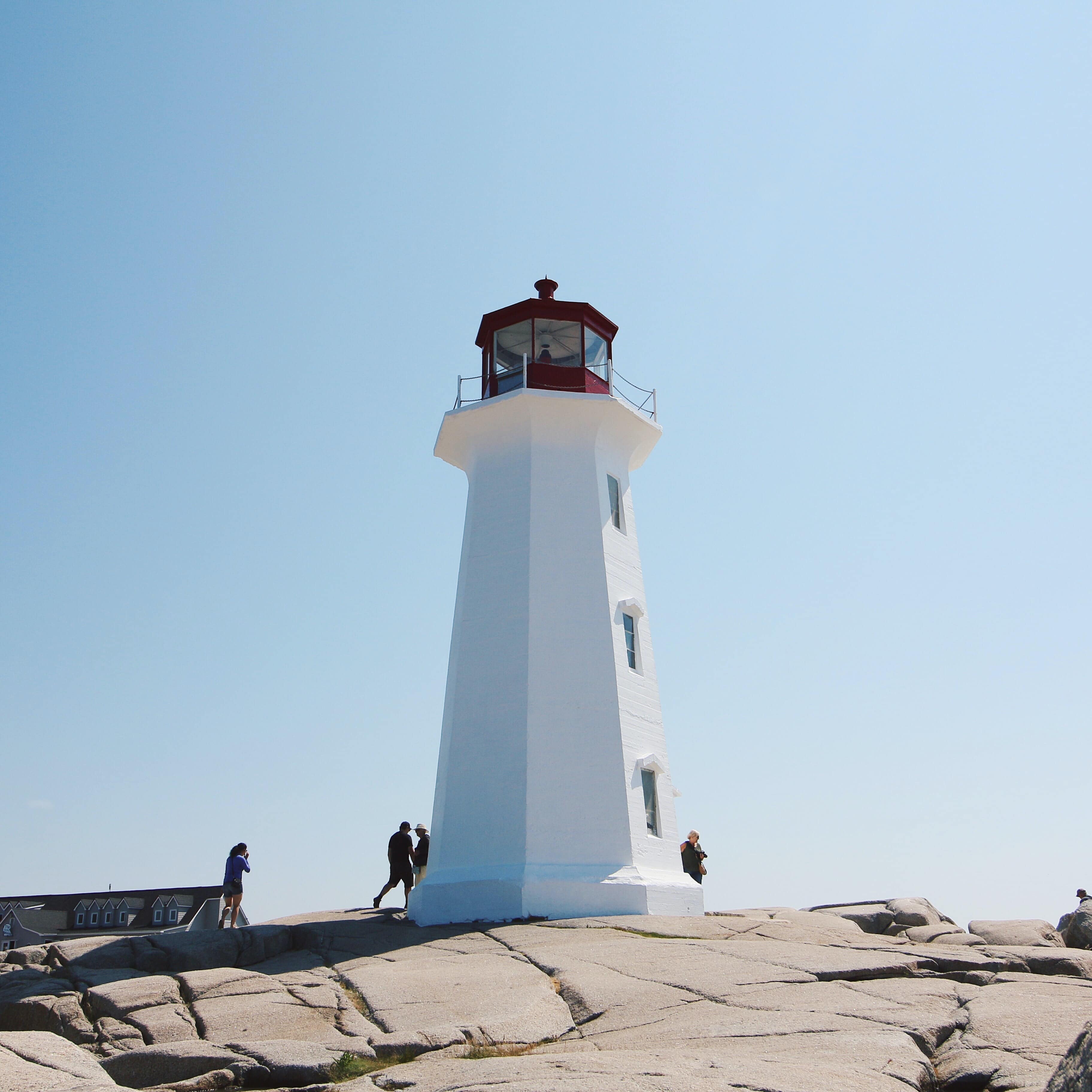 Tourists at a white lighthouse in Nova Scotia under a pale blue sky