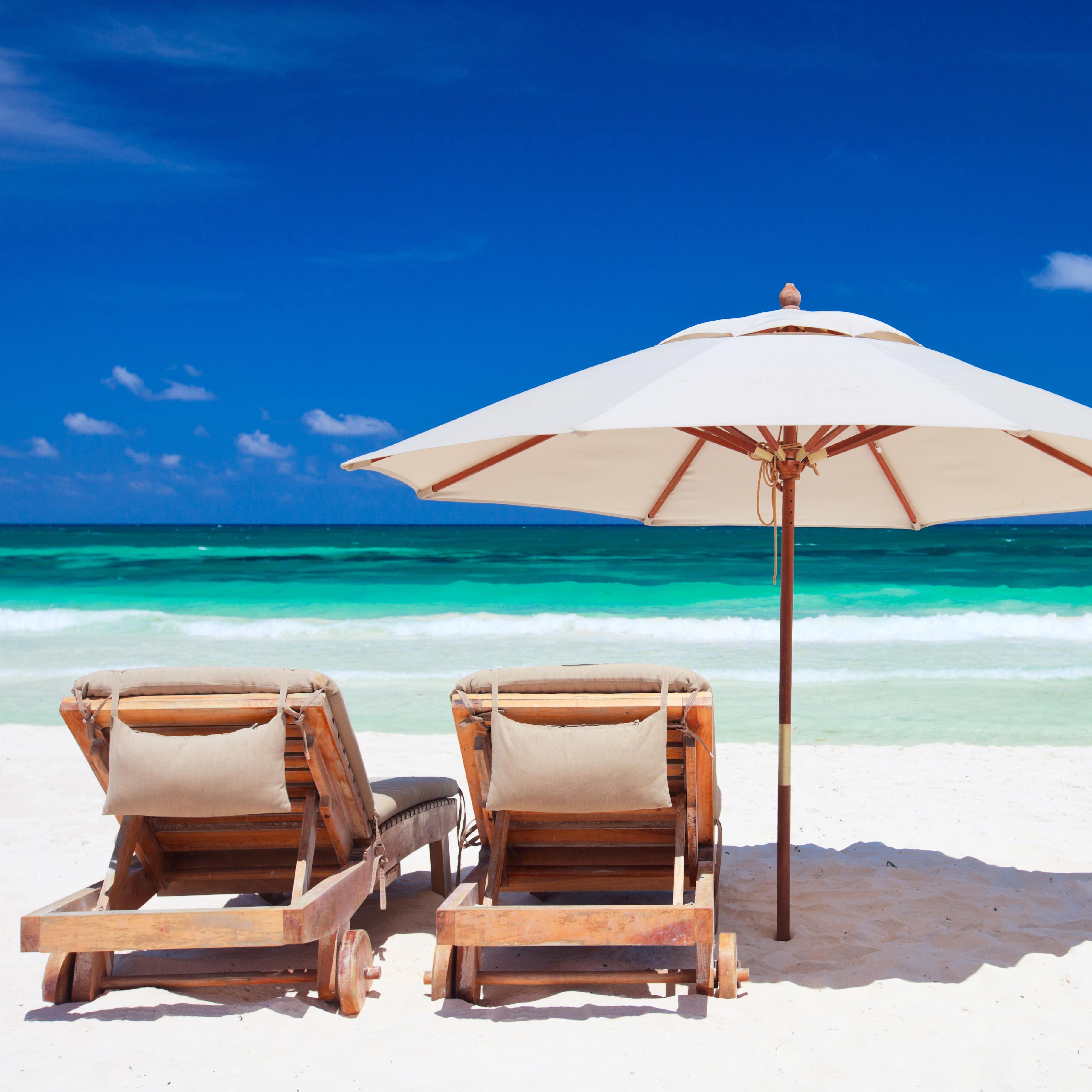 Available umbrella and chairs on a white sand beach with a turquoise ocean and blue sky in the background