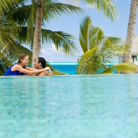 Couple in a pool with an overwater bungalow in the background