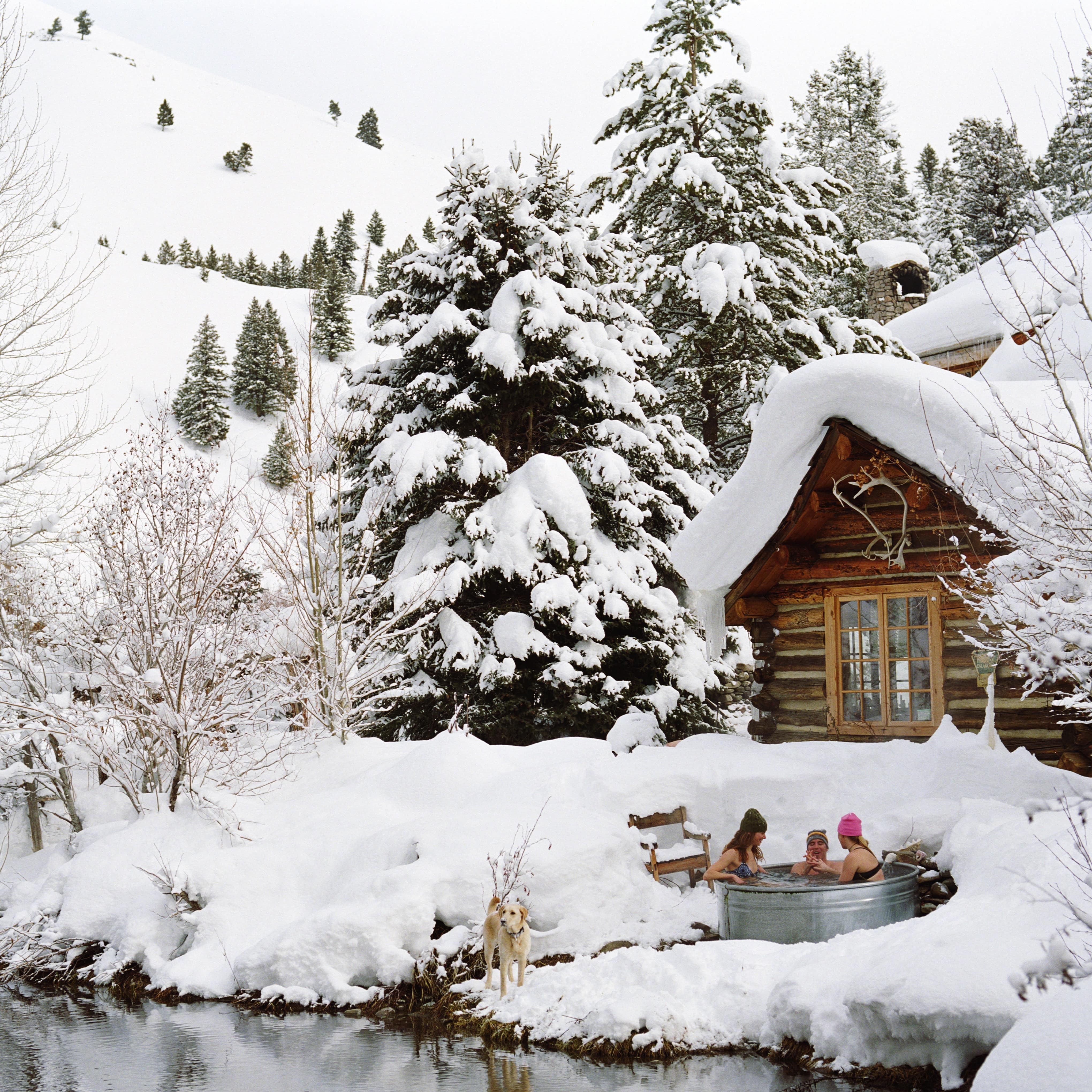 Guests in a hot tub outside a cabin surrounded by snow