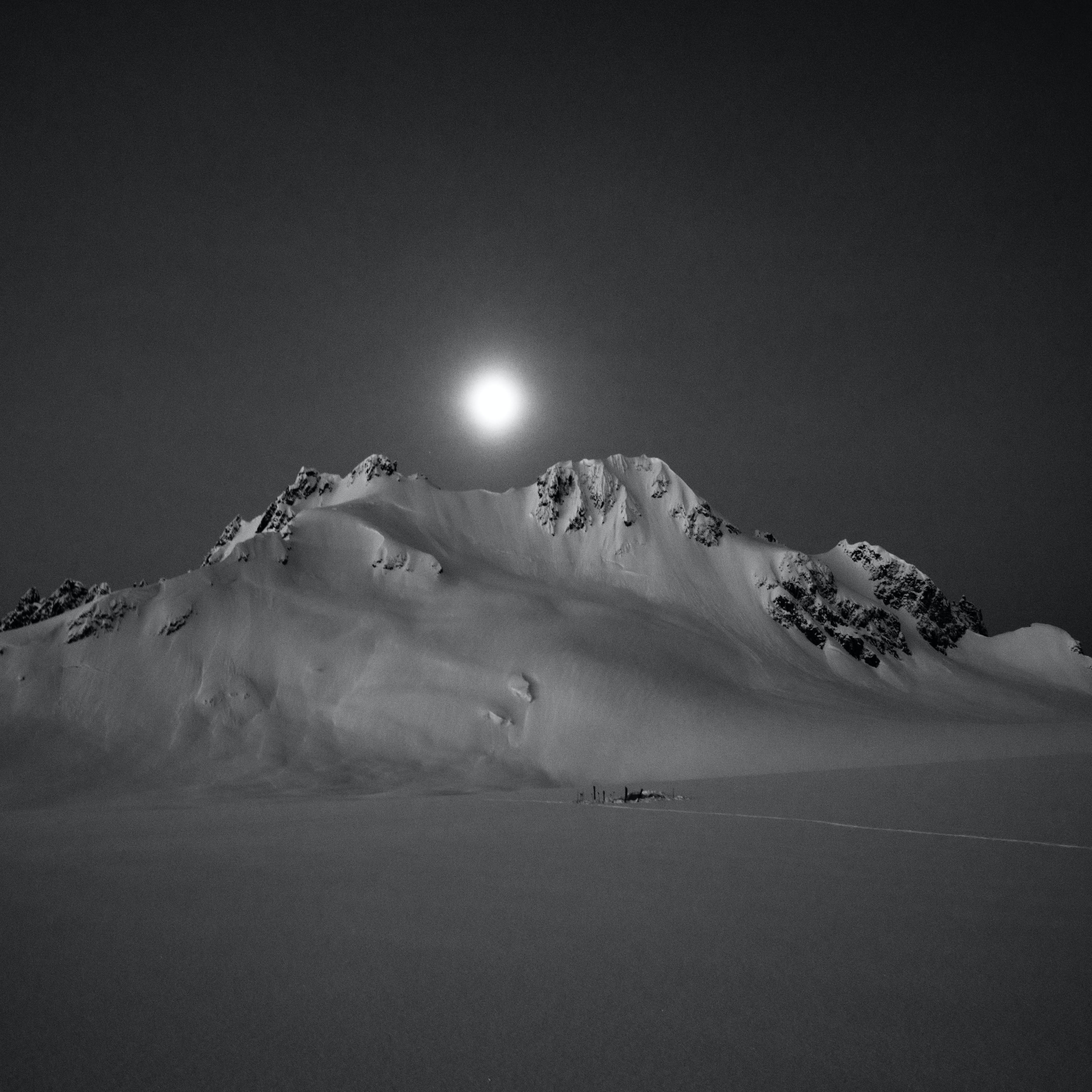 Skiers resting in their tents at the foot of a snowy mountain at night