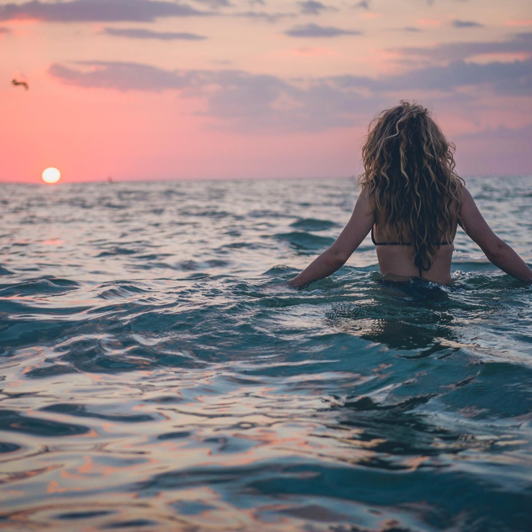 Woman wading in the water at sunset