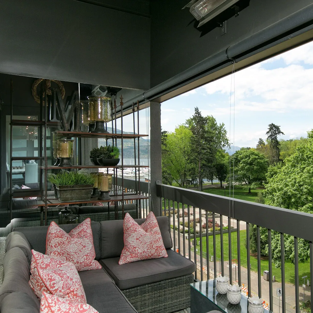 Balcony of an apartment in downtown Kelowna furnished with a couch ooking out on trees and the harbour in the distance