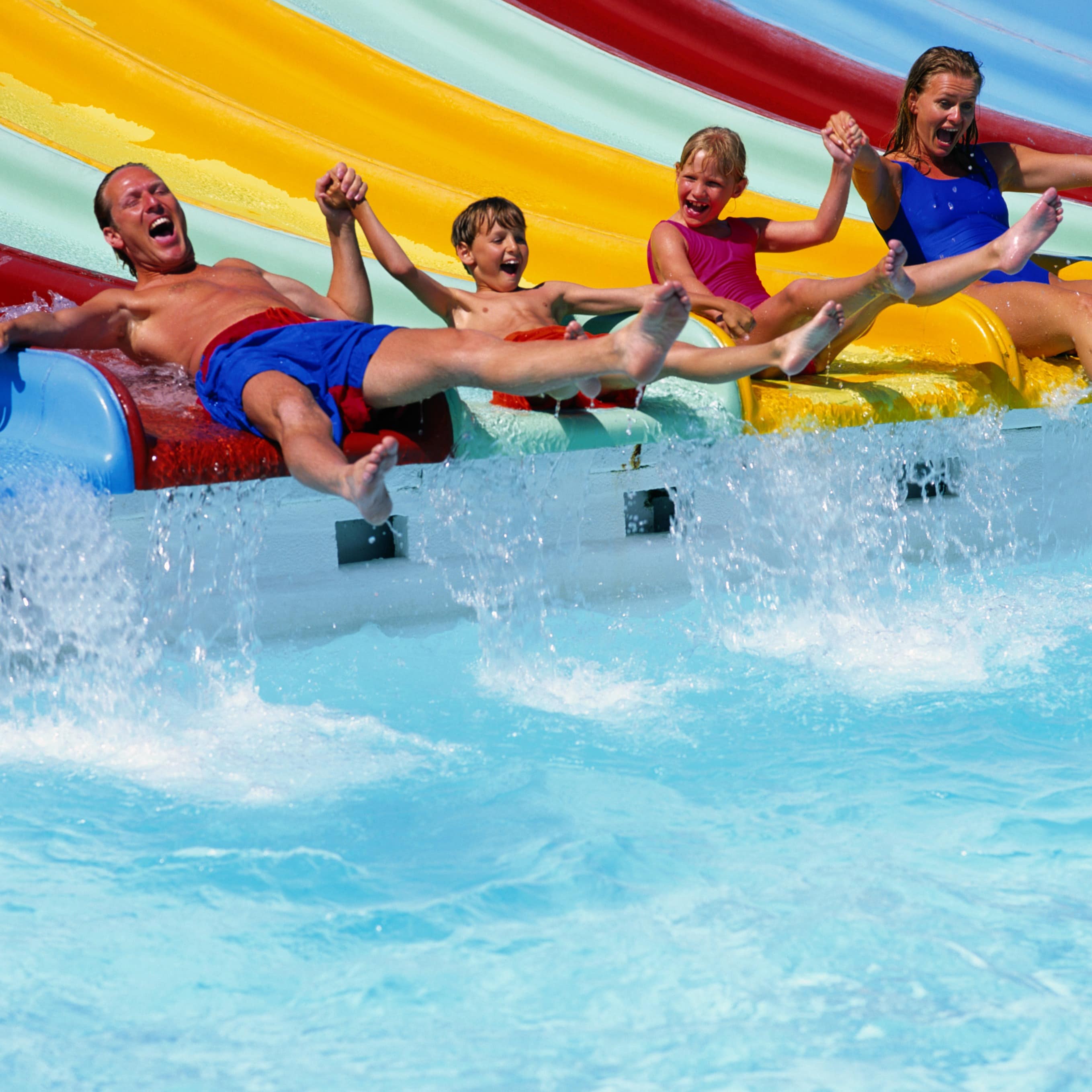 Mom and dad sliding down a waterslide with their two kids into a pool!