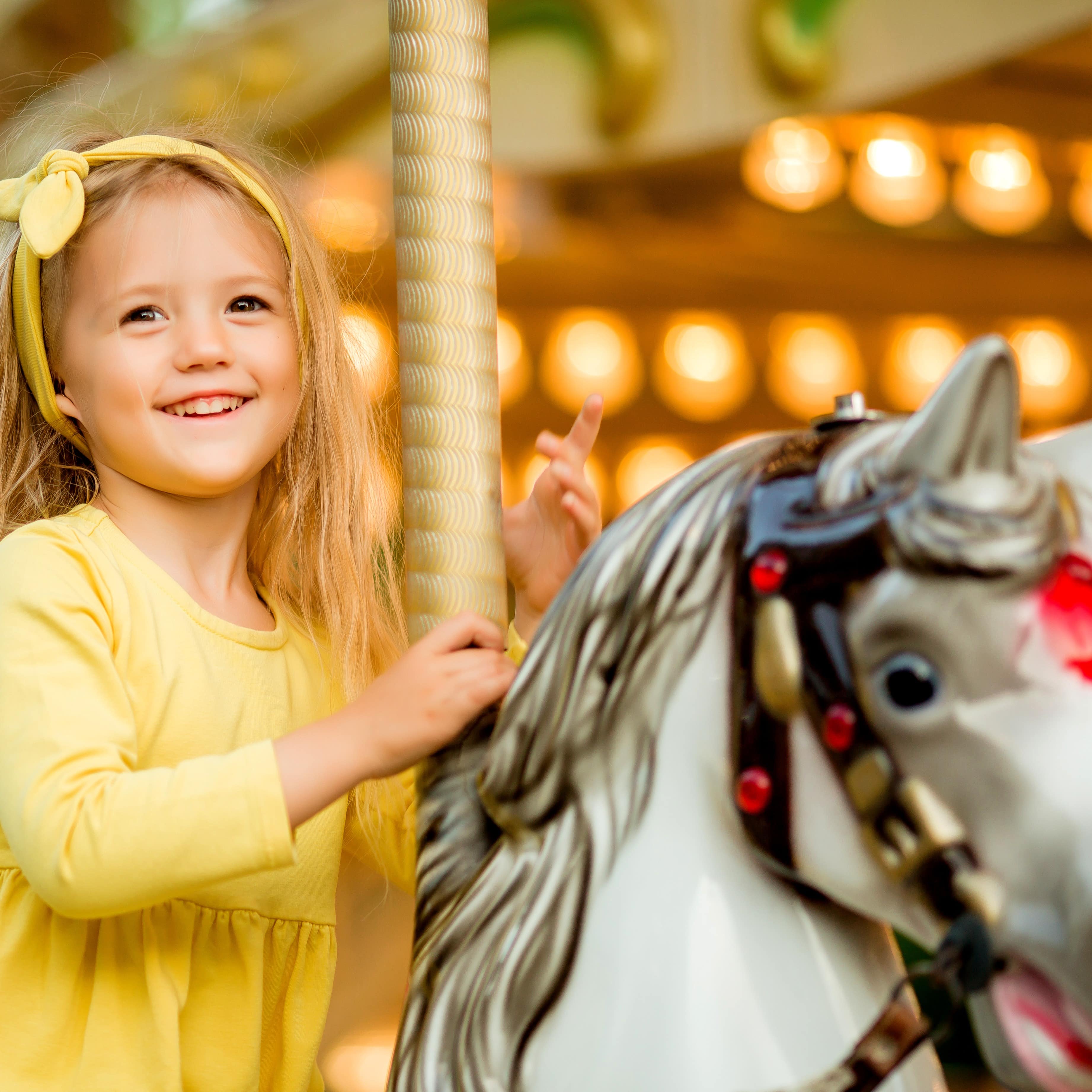 Little girl in yellow top riding on a carousel