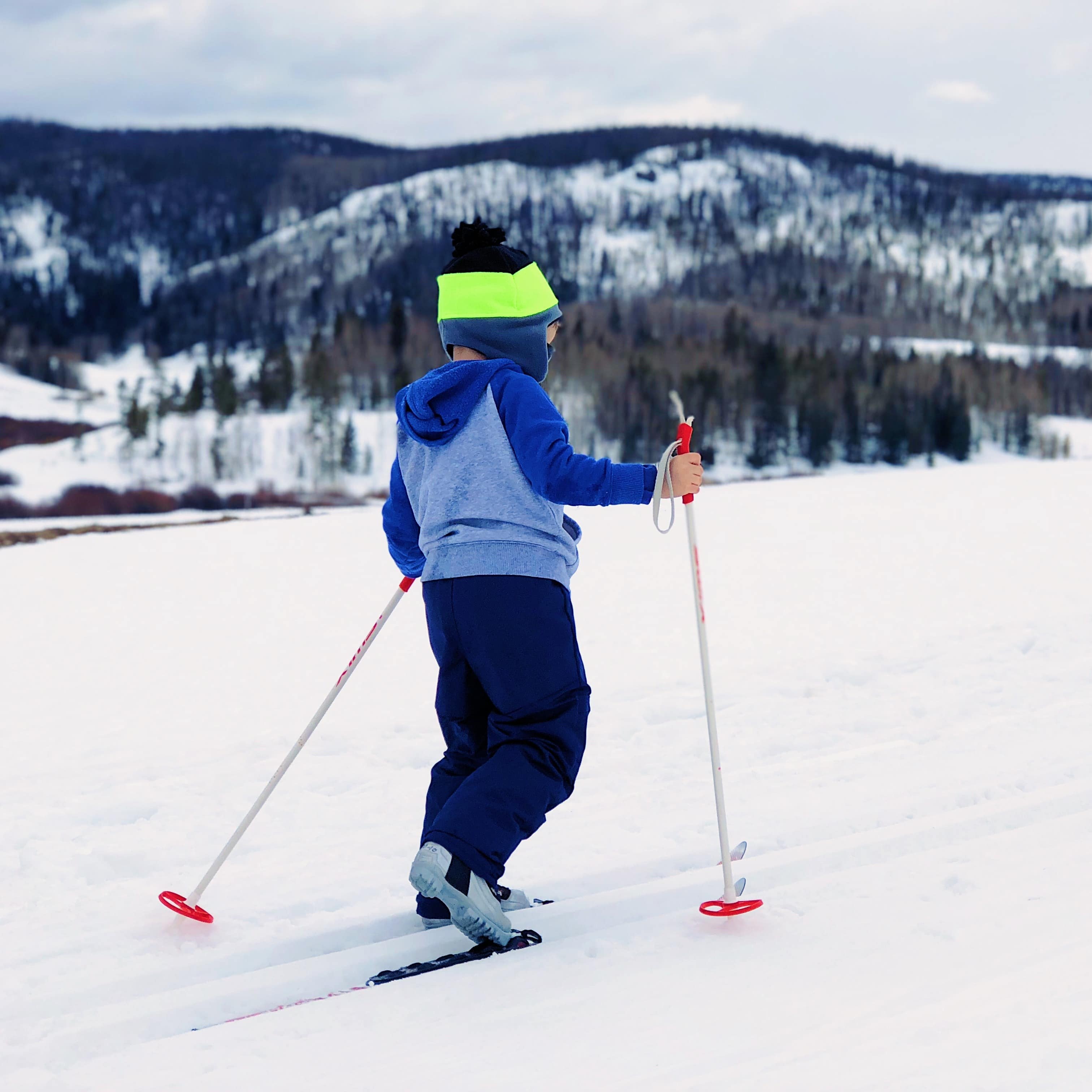 Child with ski poles in front of snow-covered mountains