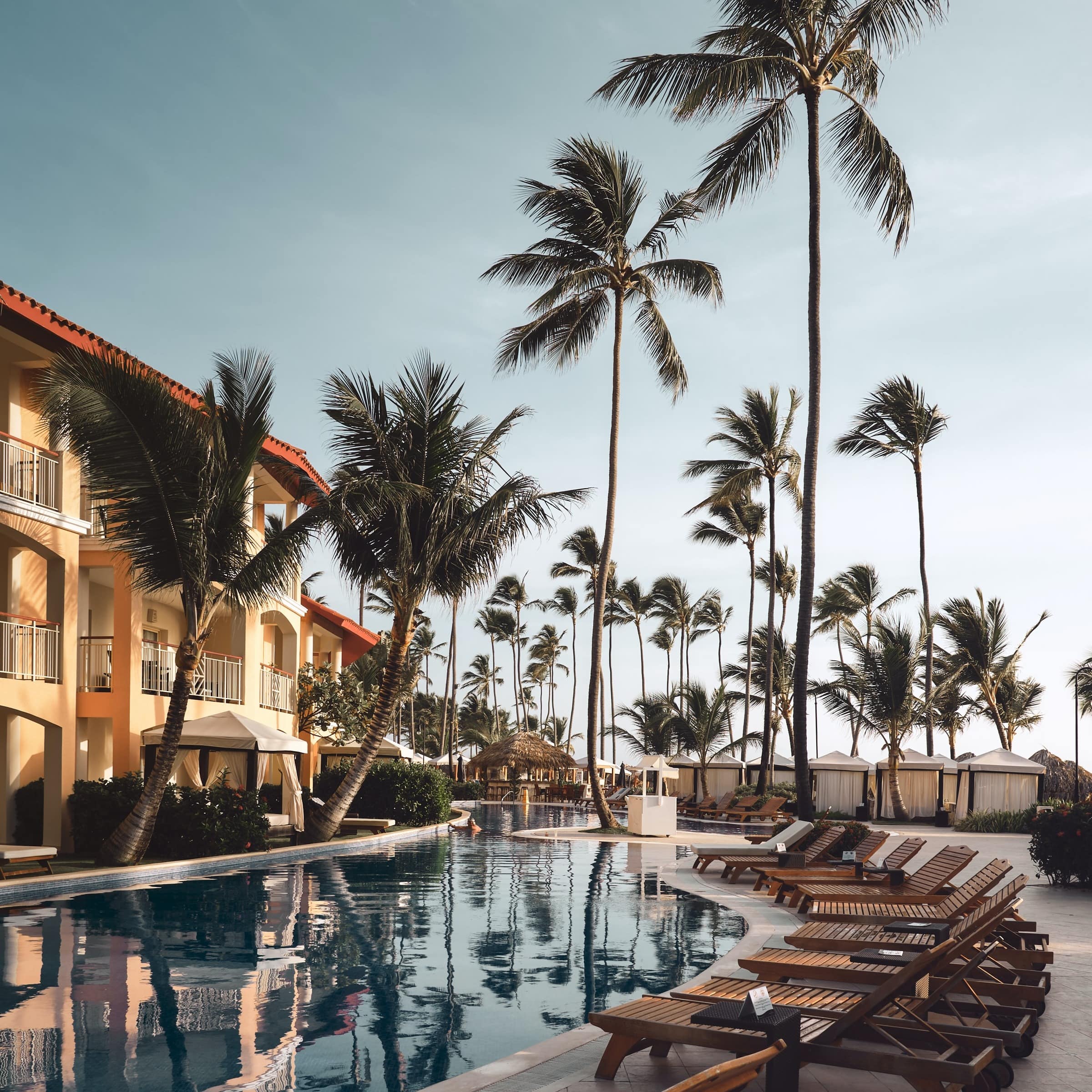 Brown lounge chairs and palm trees surrounding a beachfront hotel’s private pool