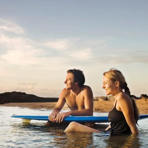 Couple sitting in the water with a blue surfboard