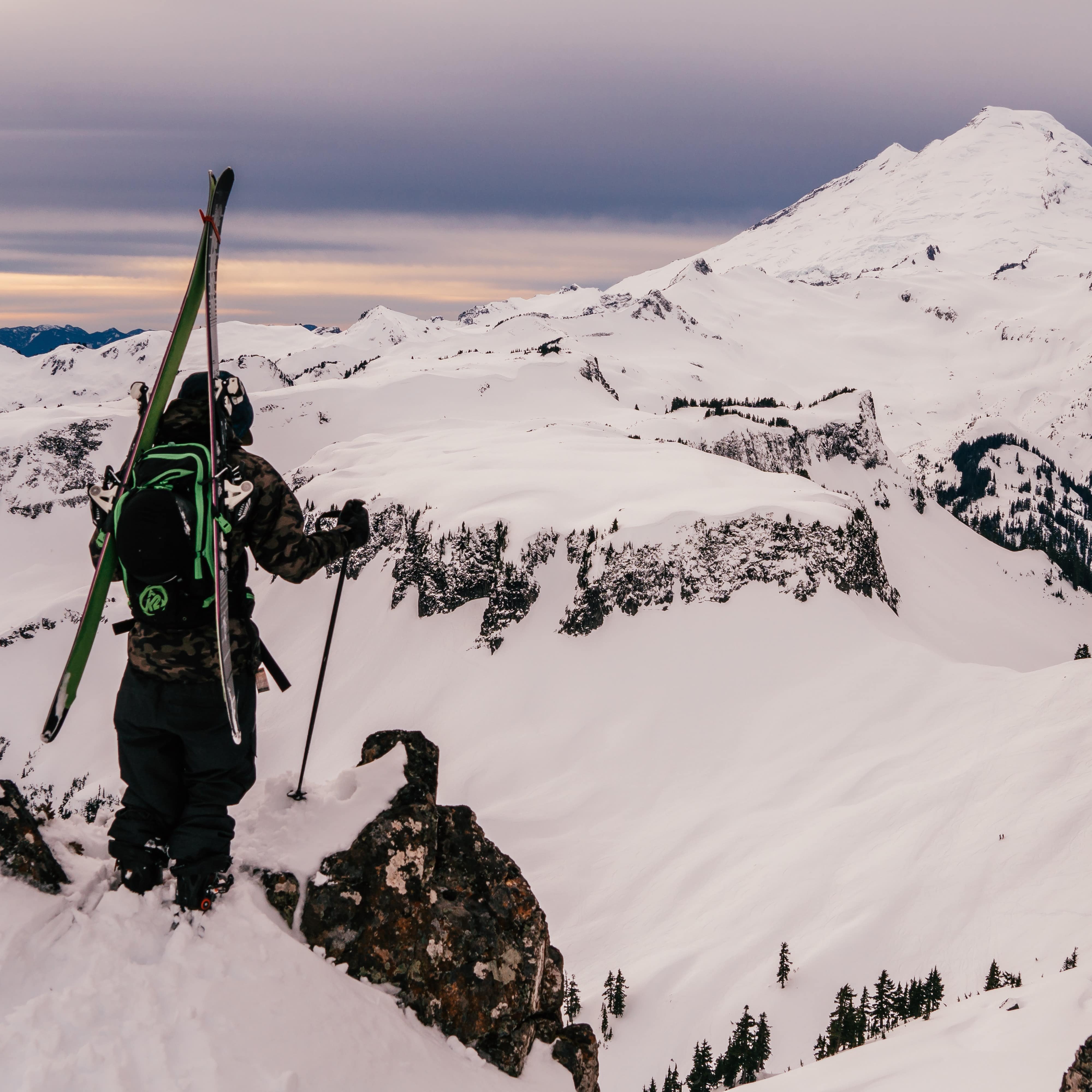 Skier standing on top of a snow-covered mountain looking down at rough terrain