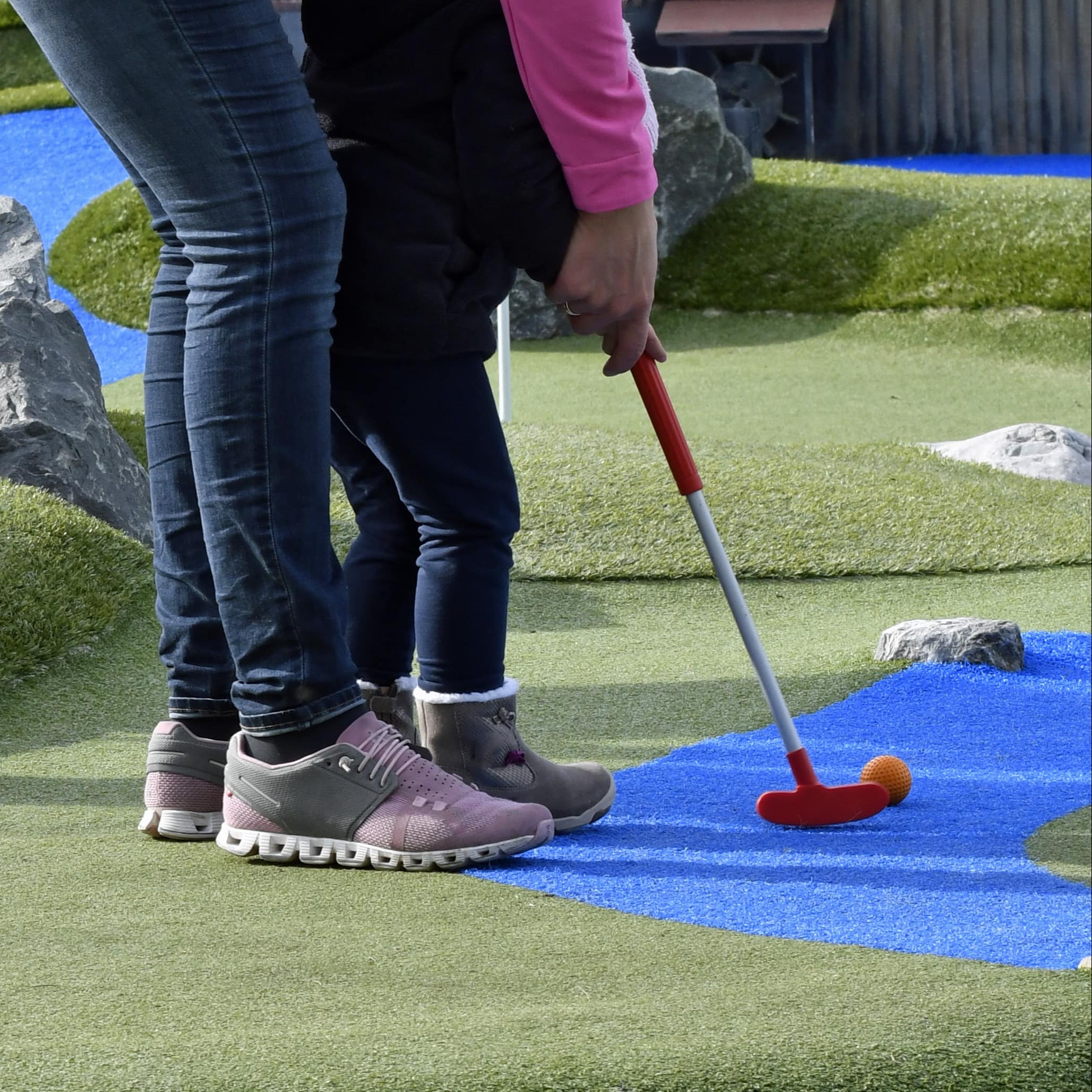 Parent helping a toddler play mini golf
