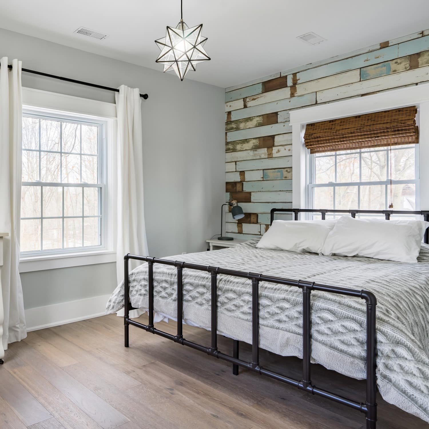 A spacious bedroom with hardwood floors, wood-panelled accent wall, a king size bed, and rustic decor.