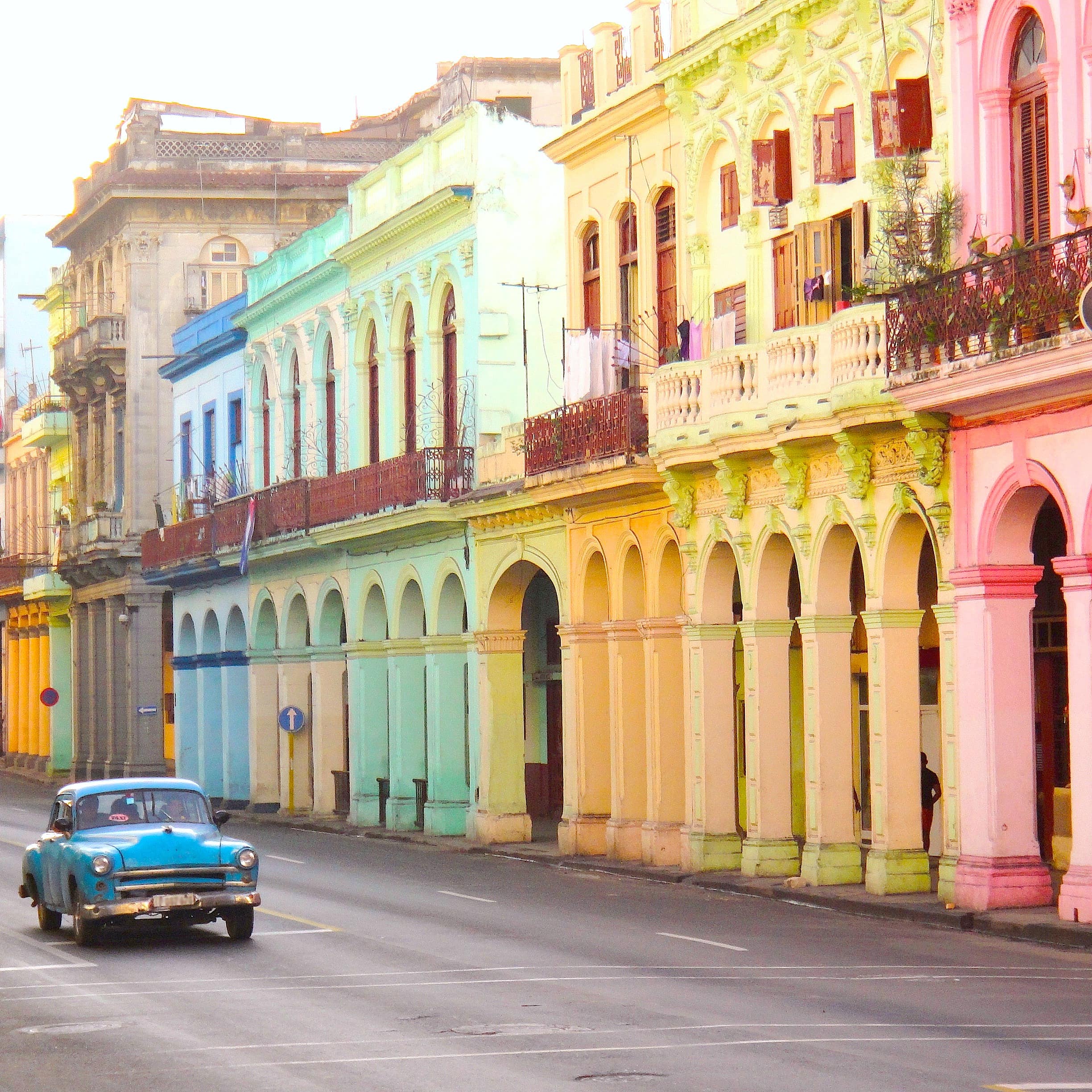 A blue cadillac driving through the streets of Havana, Cuba lined with colourful pastel buildings