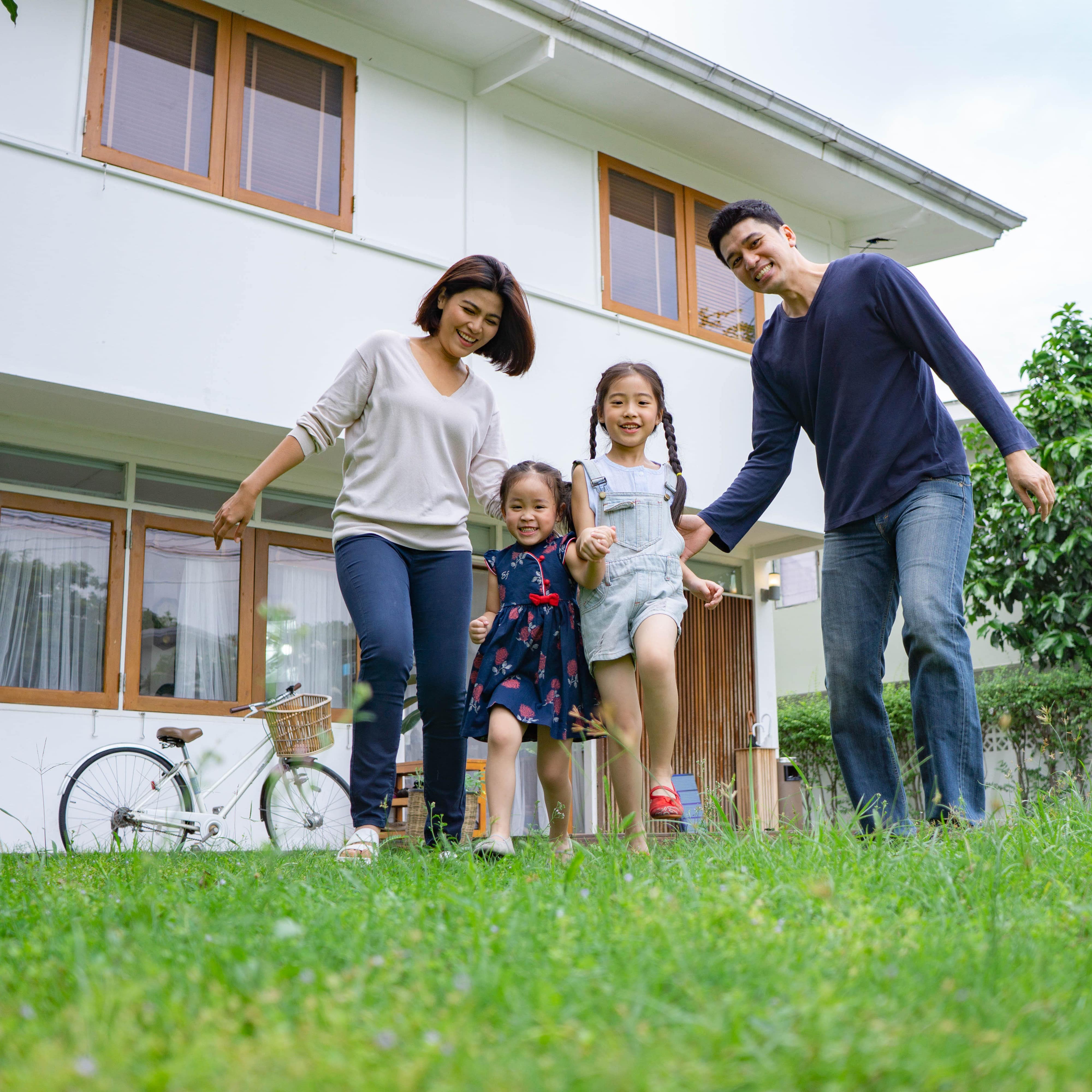 Smiling Asian family running toward camera after a bike ride with a house in the background