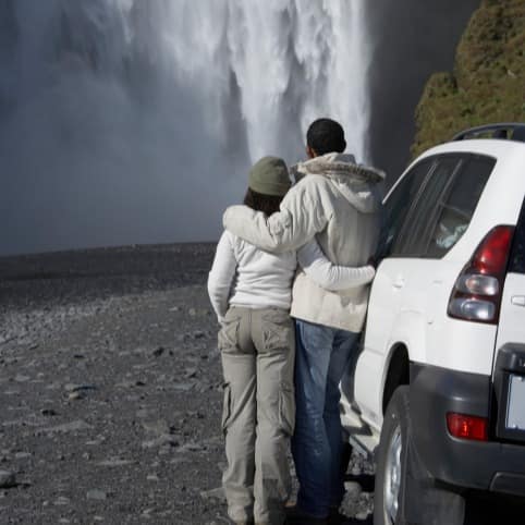 A couple looking at a waterfall in the distance from outside their car