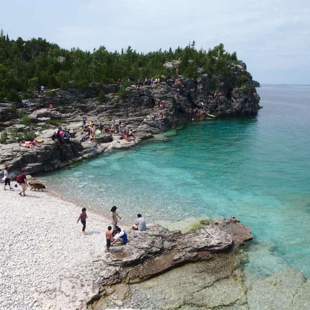 Families play on a rocky beach and cliffs by crystal clear water.
