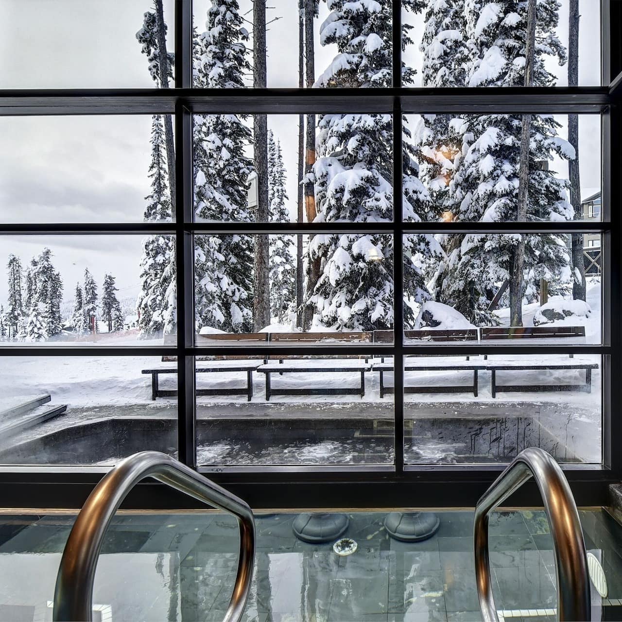 View of the indoor and outdoor hot tub and pool areas with a snowy background through the windowed walls