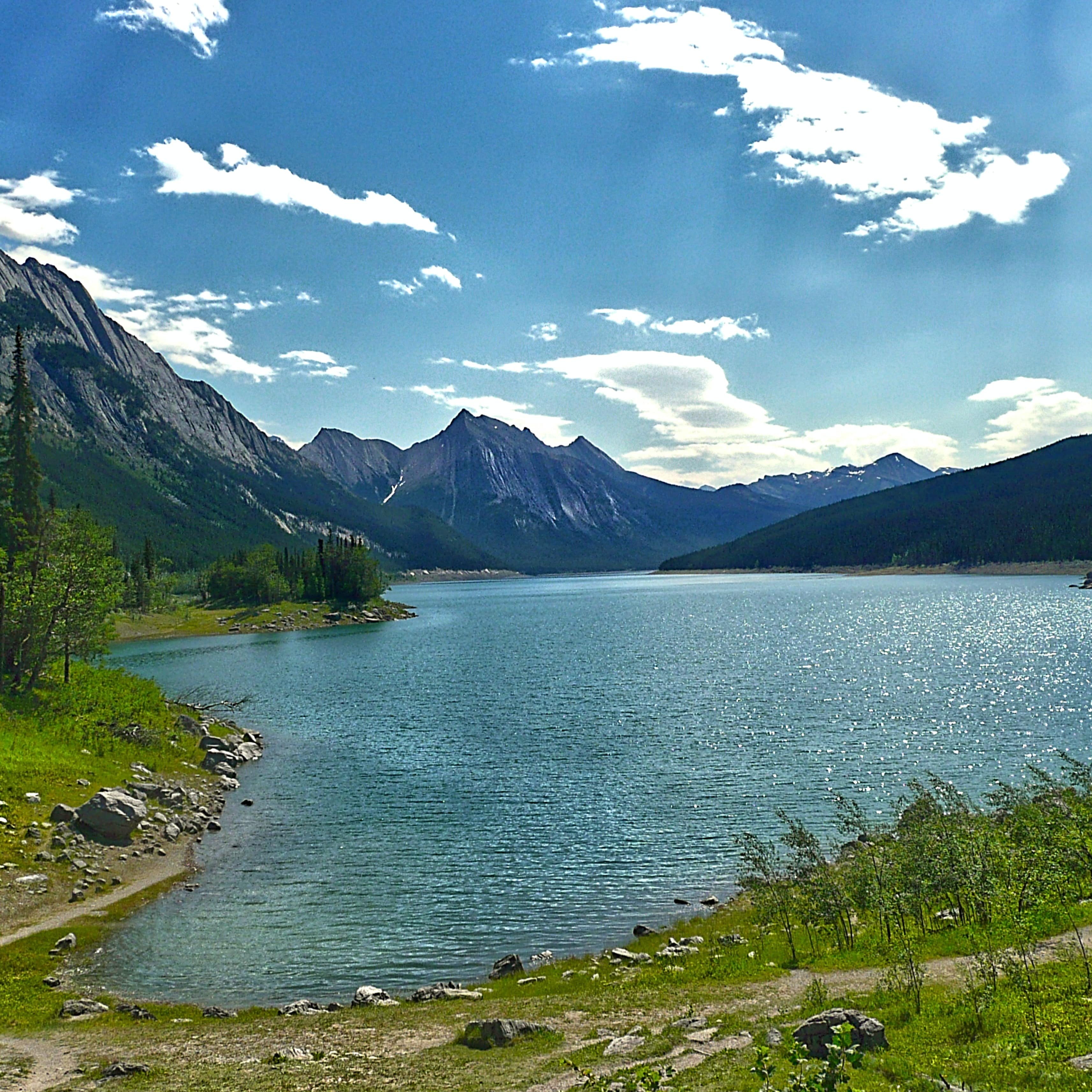 Medicine lake surrounded by green trees and mountains under a blue sky