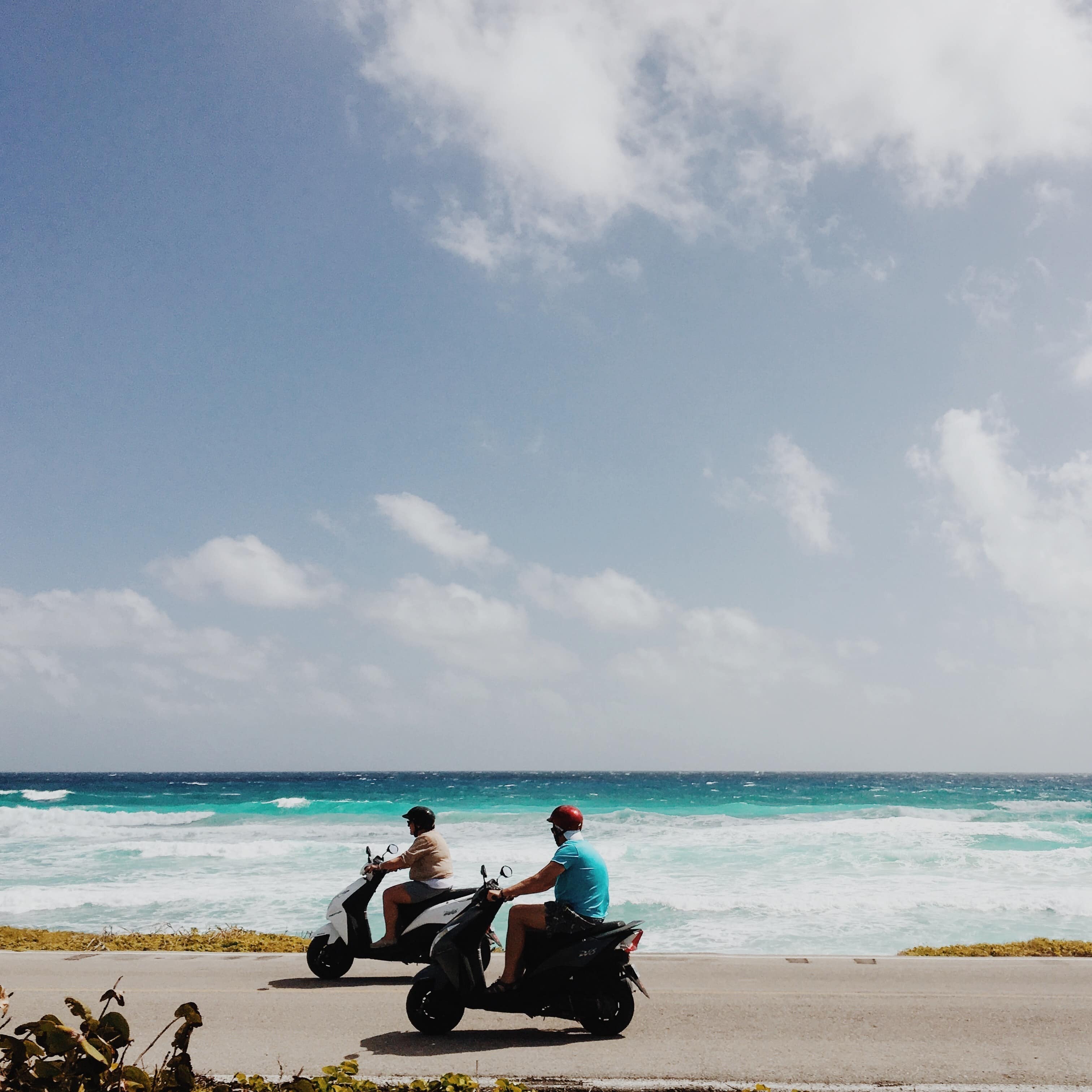 Two people riding scooters on the coast of Cozumel with the bright ocean waters in the background
