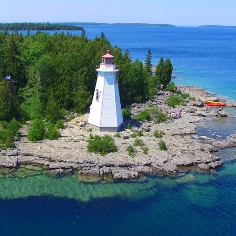 Aerial view of a white and red lighthouse on a rocky island. 