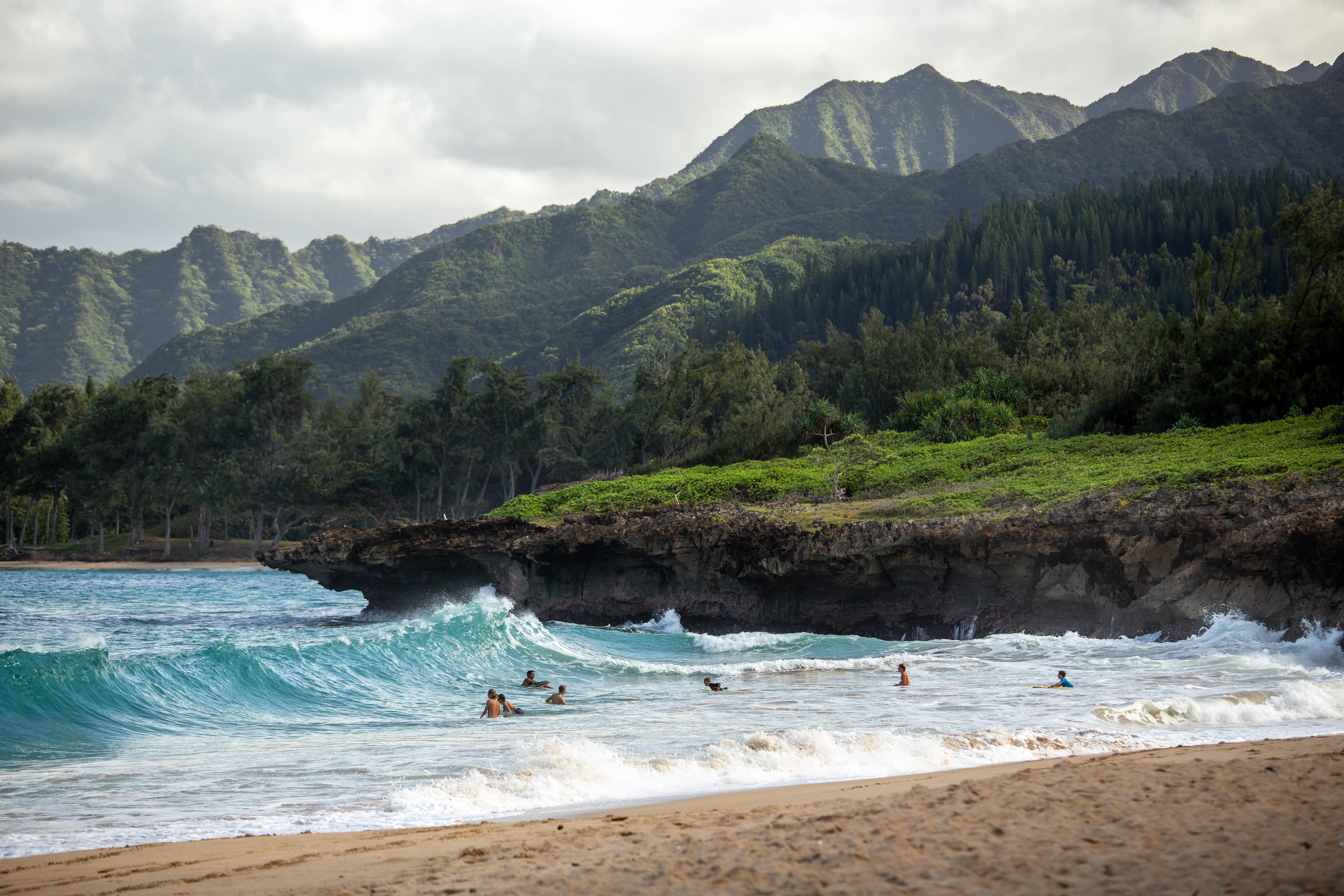 People swimming off the shores of Hawaii as the waves crash on the sand