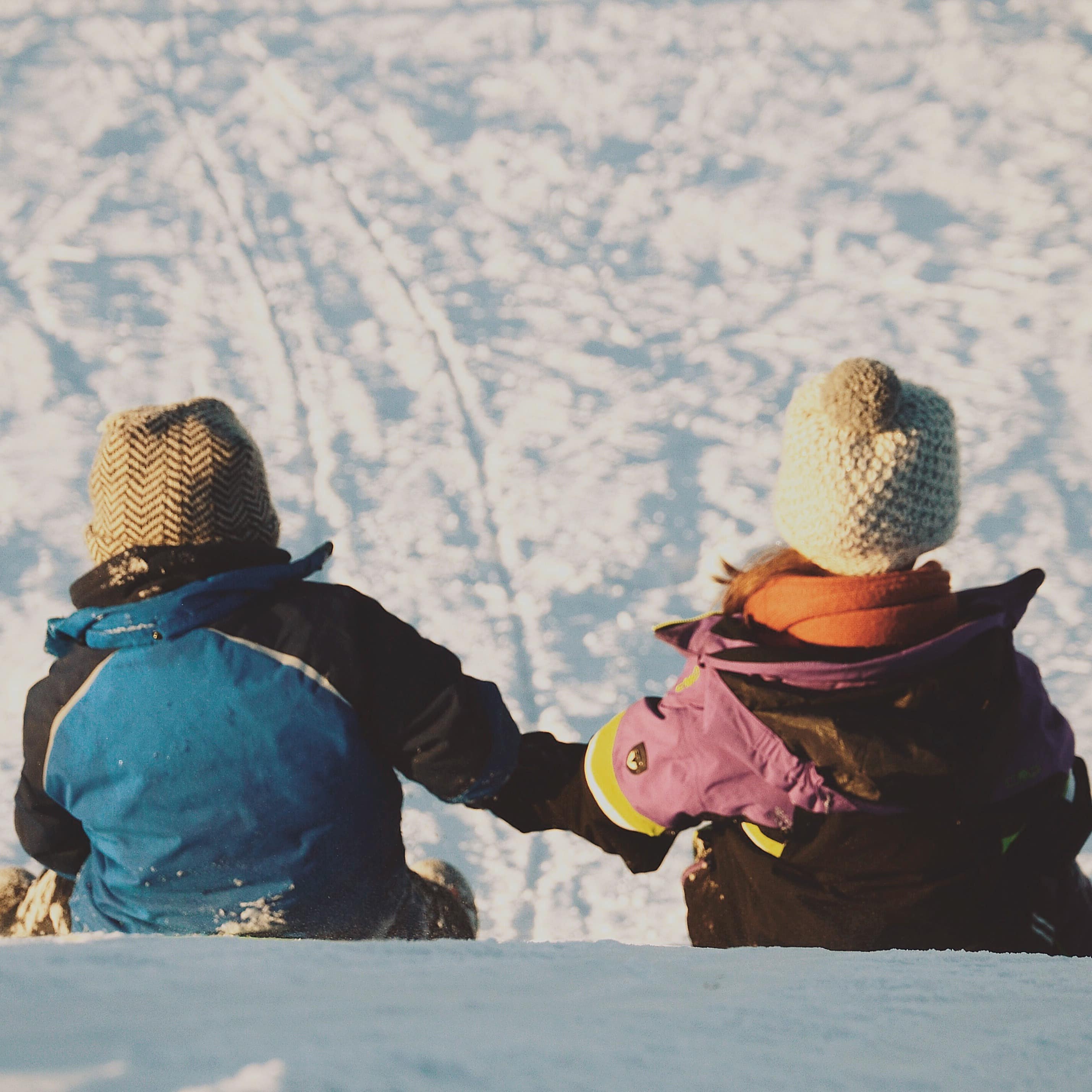 Children holding hands sitting on a ski slope