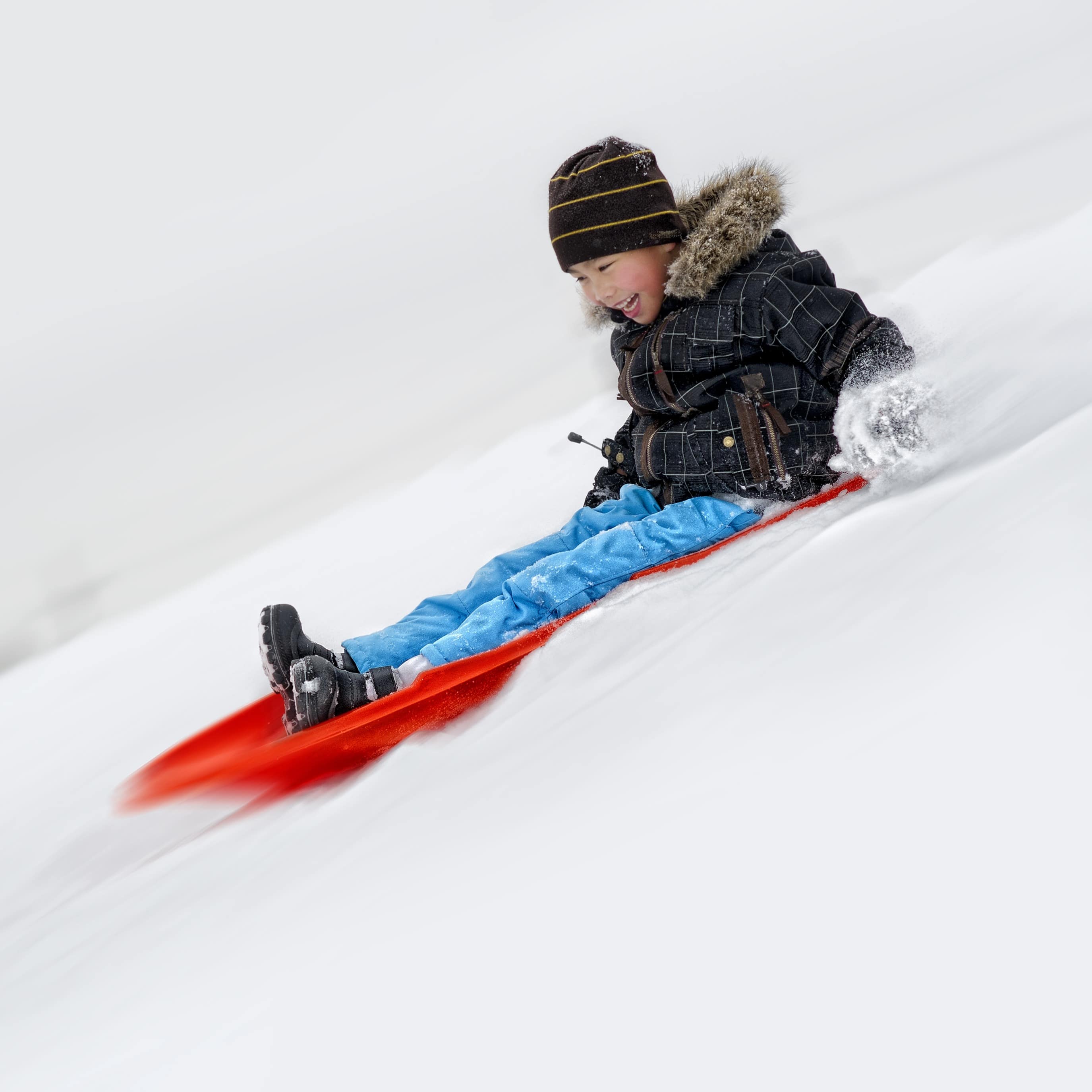 Happy child coming down the ski slope on a red sled