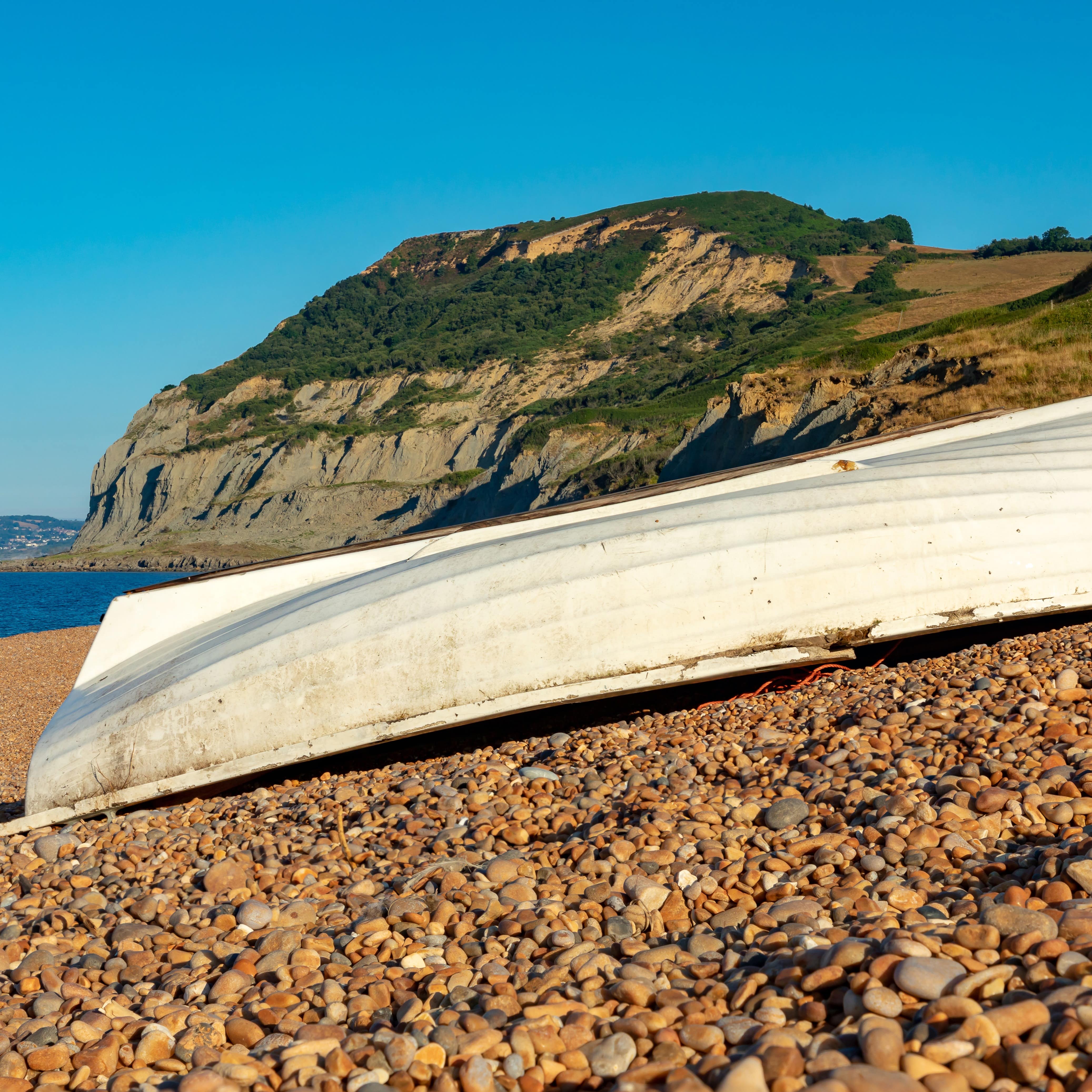 Upside-down white fishing boat on the pebbled beach of Seatown in Dorset