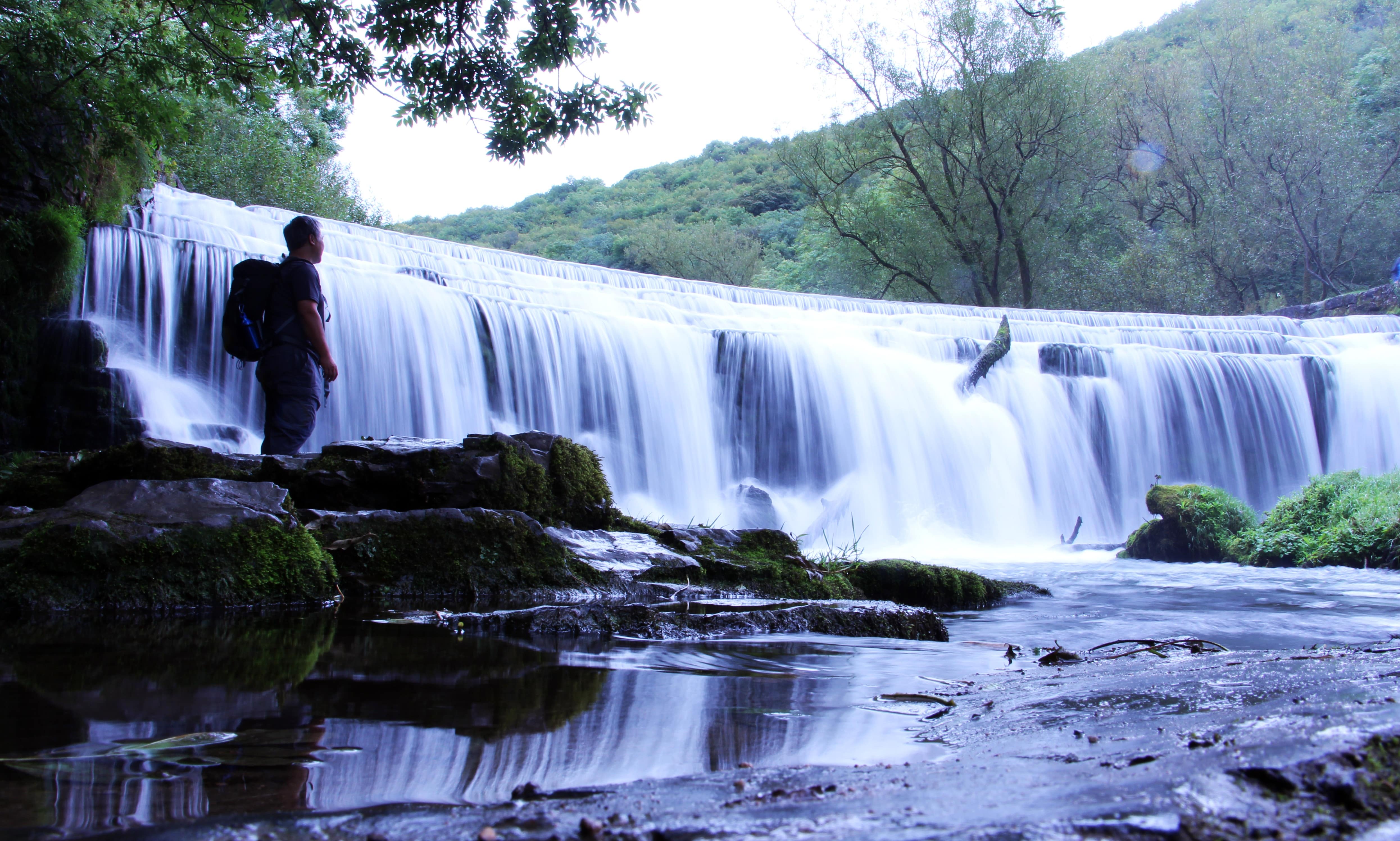 A hiker watches a waterfall in the Peak District