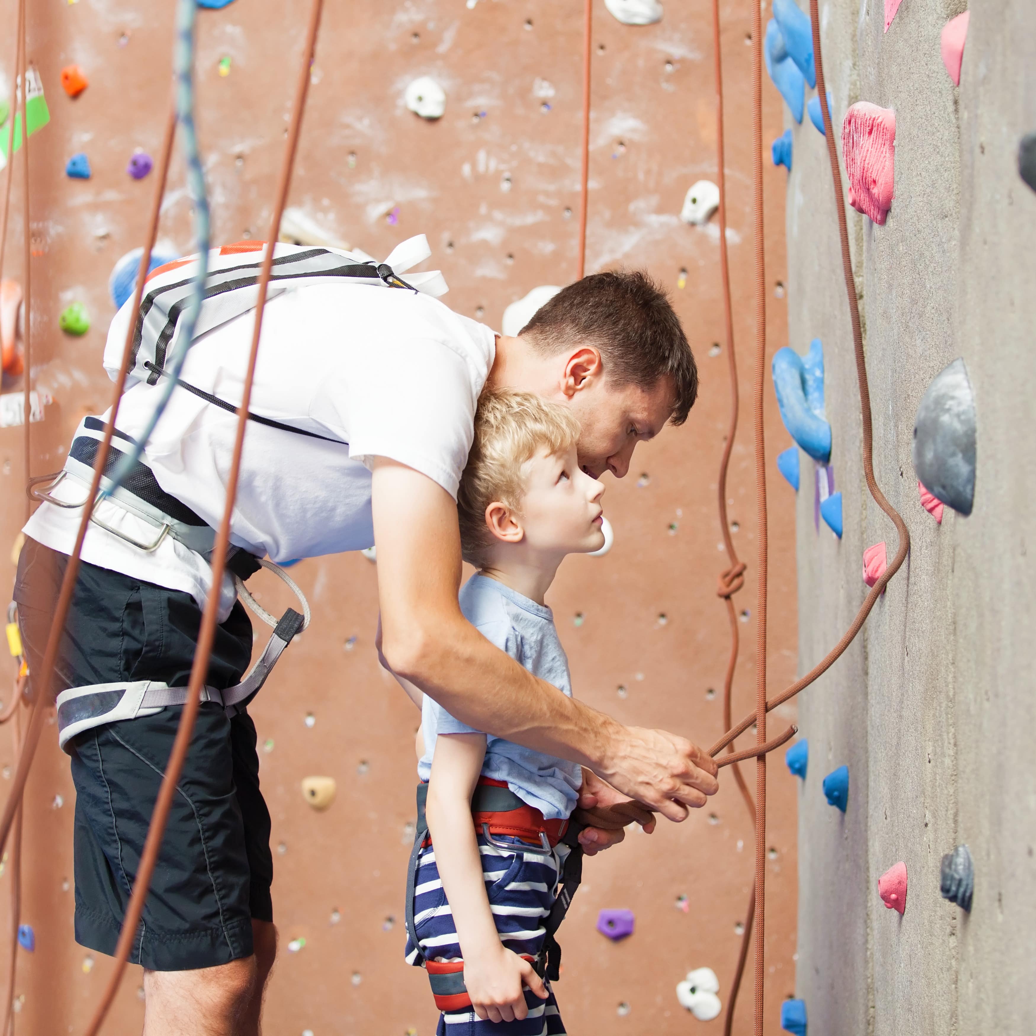 Father roping in his son to climb a rock wall
