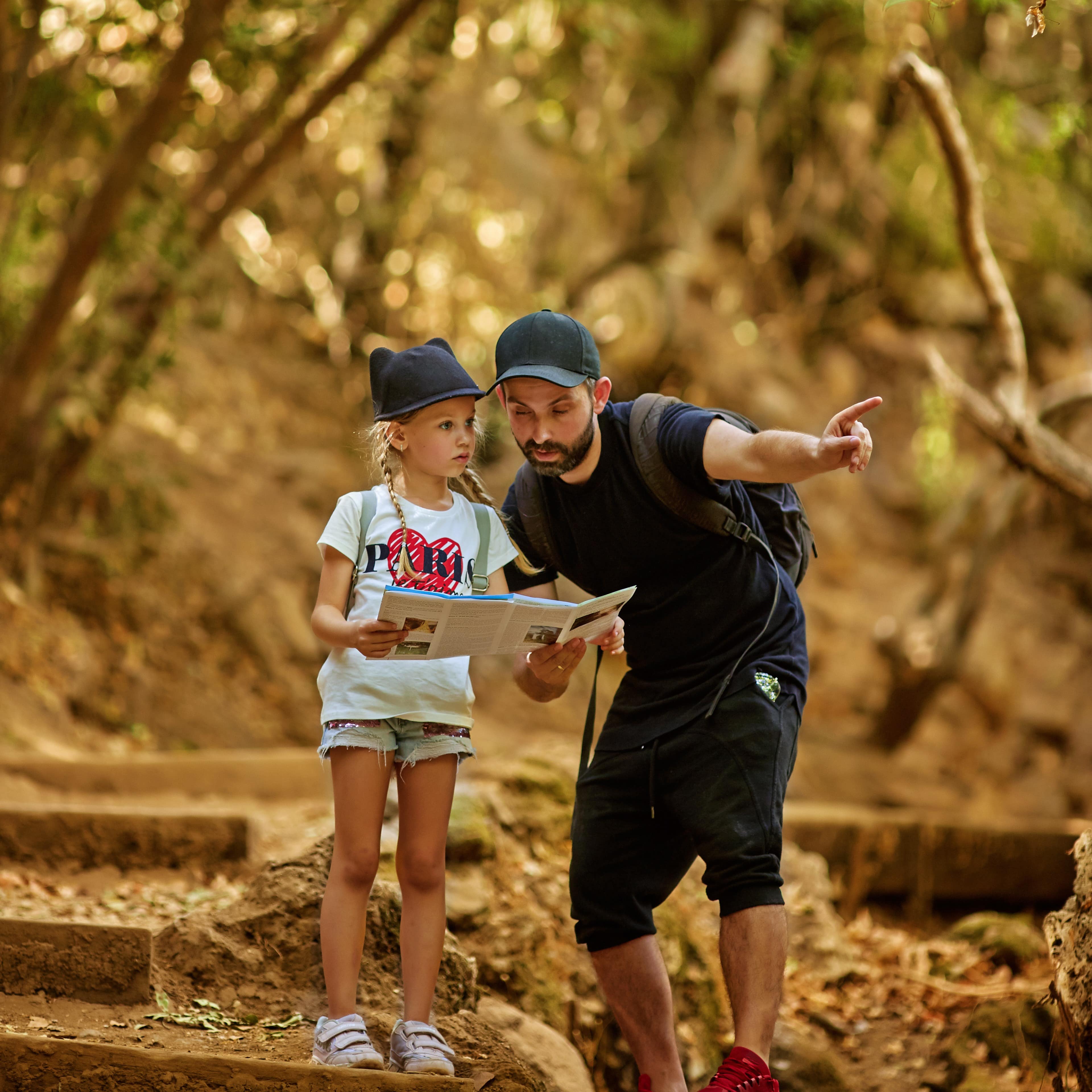 Dad pointing and reading a treasure map in forest with his young daughter