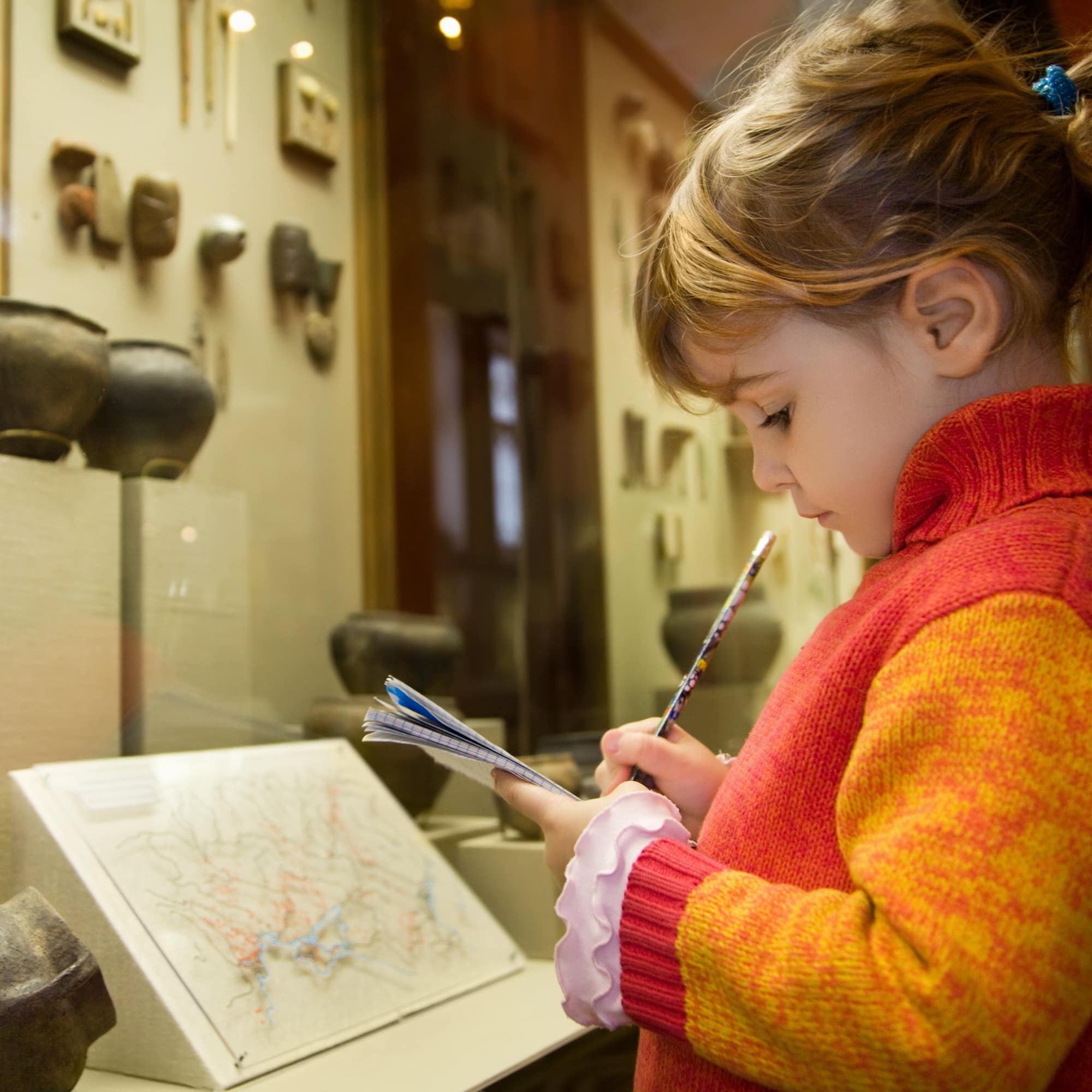 Little girl writes in notebook at an excursion in a museum