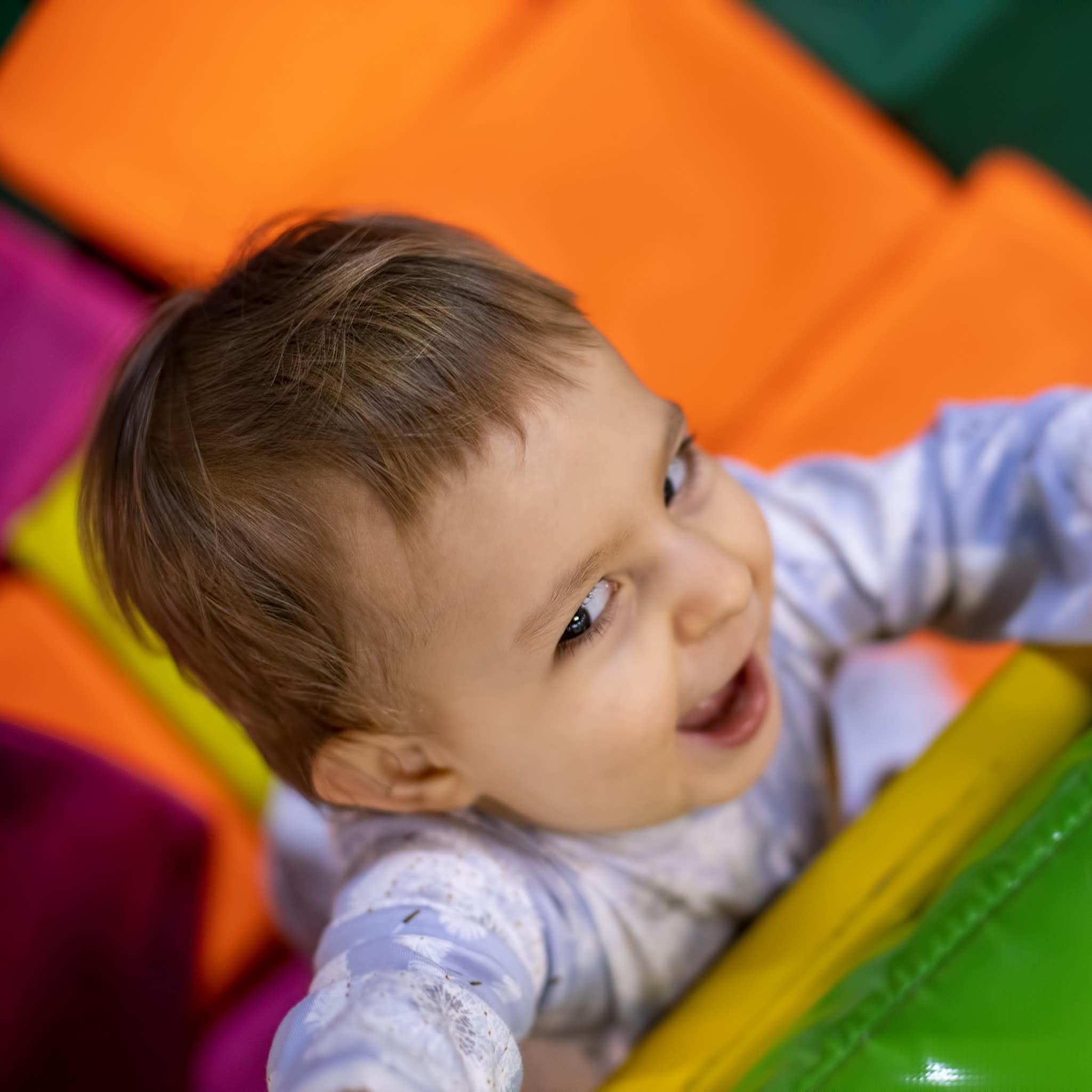 Young toddler smiling as she climbs out of pool of soft cubes in play centre