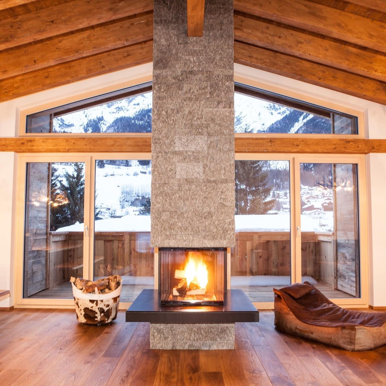 Fireplace centred in a living area of a chalet in Tyrol, Austria, with views of the snowy mountains through the glass 