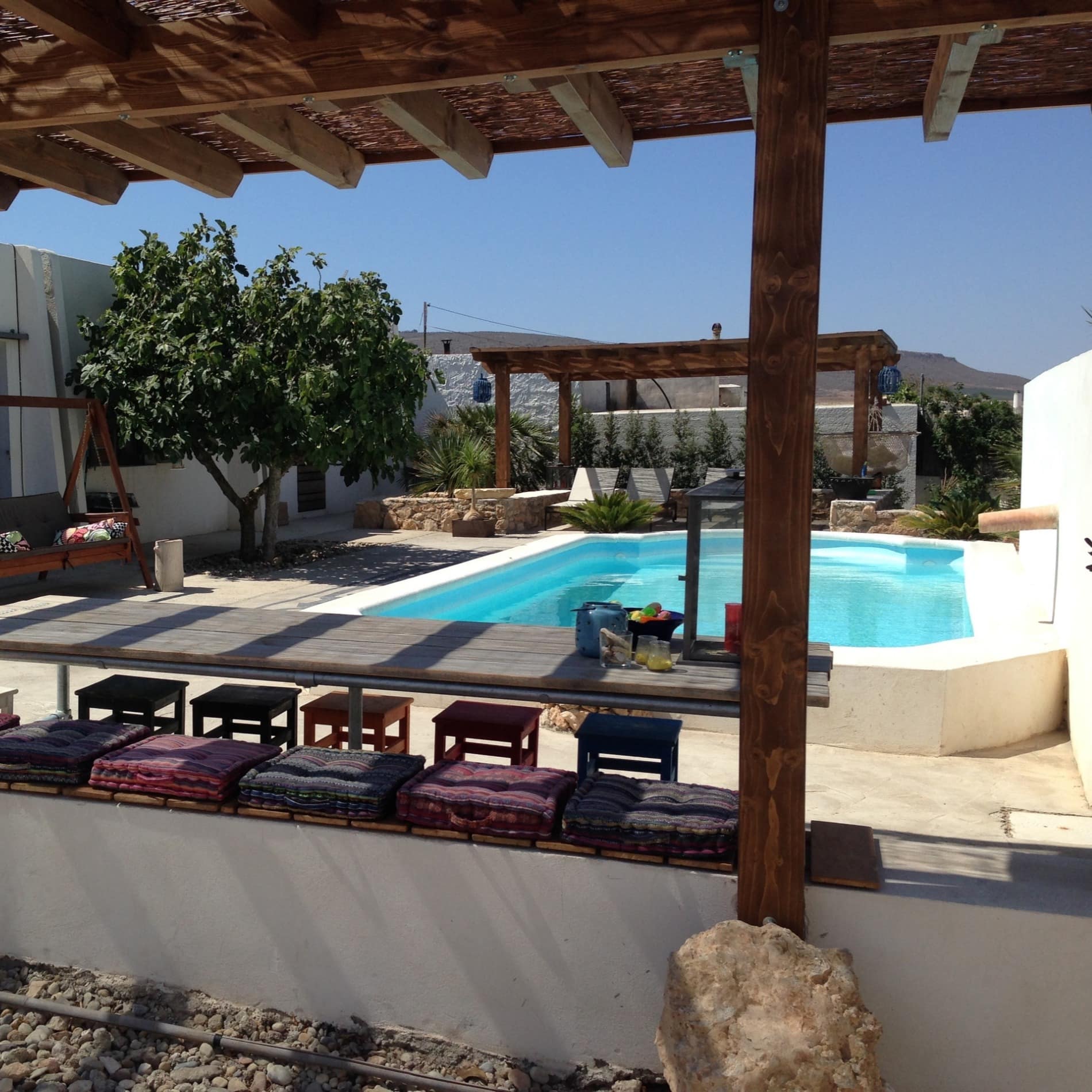Jardín de una casa de campo entre montañas con piscina, mesa y asientos de distintos tipos