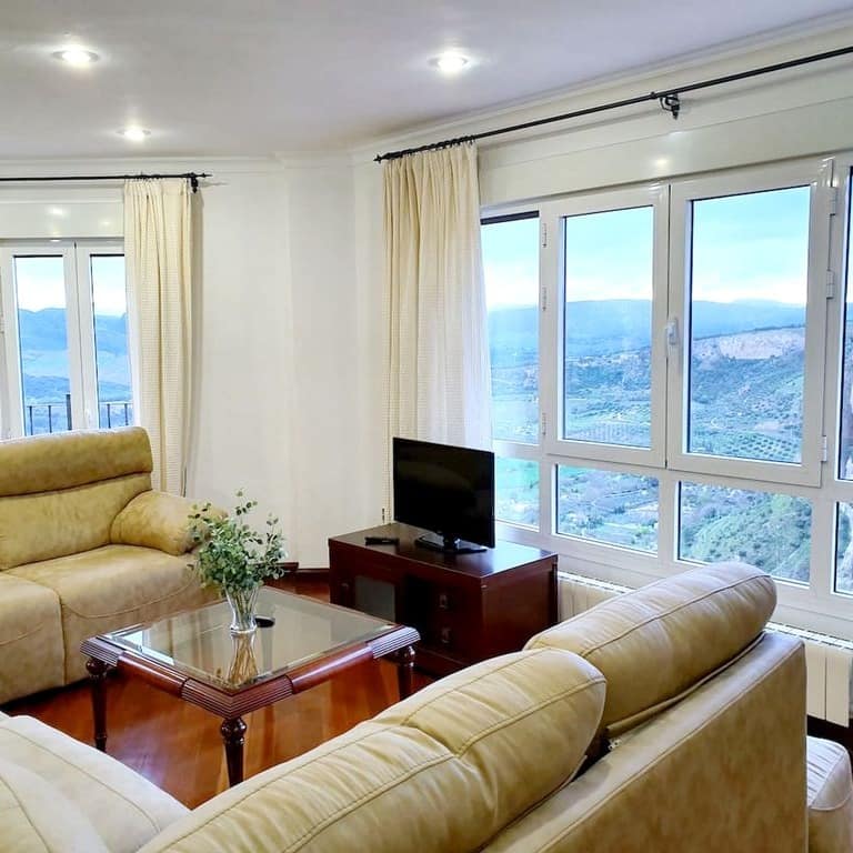 Comedor con sofá y televisión ante un ventanal con vistas al paisaje de Ronda