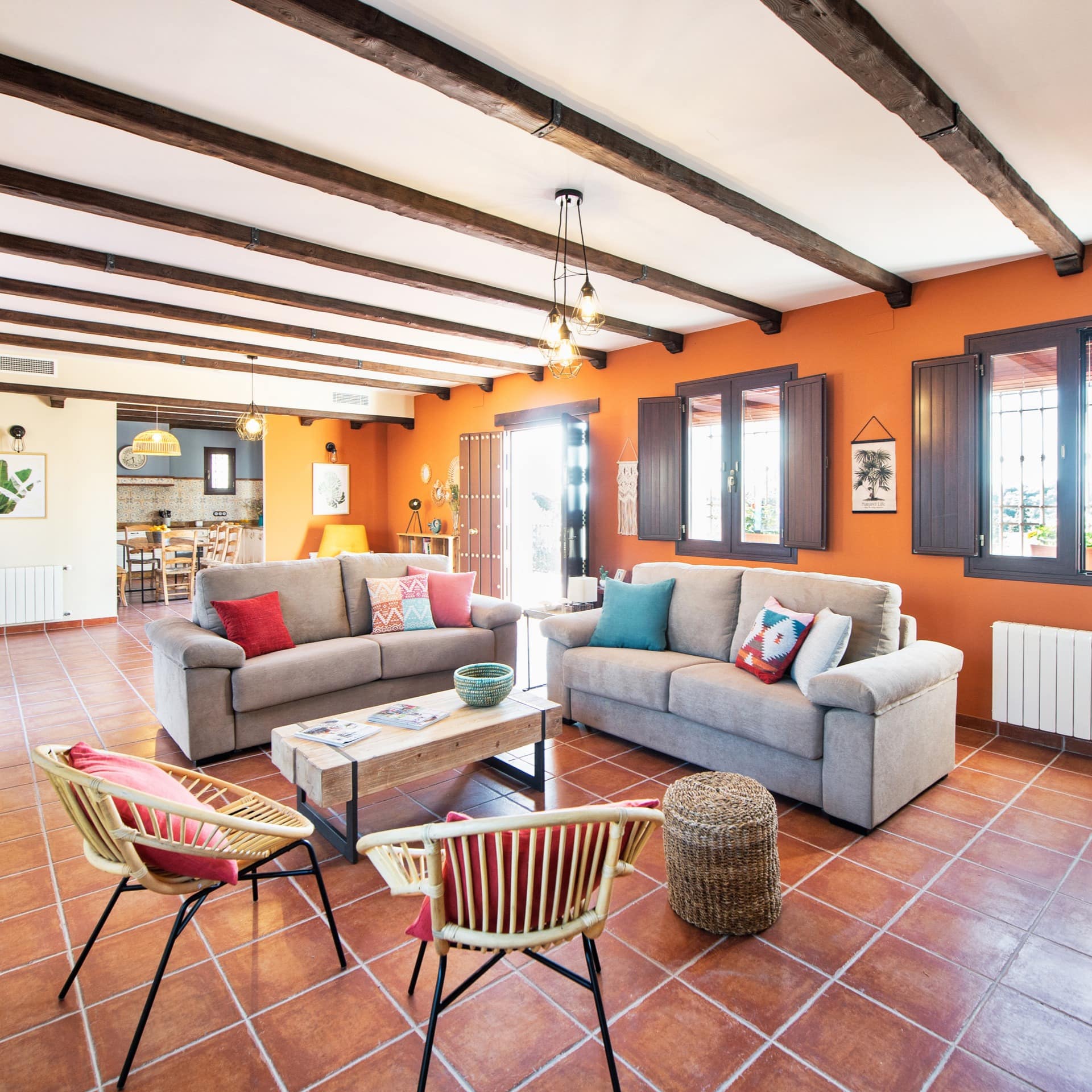 Salón de casa de campo con suelo de cerámica, vigas de madera en el techo y ventanas con postigos oscuros