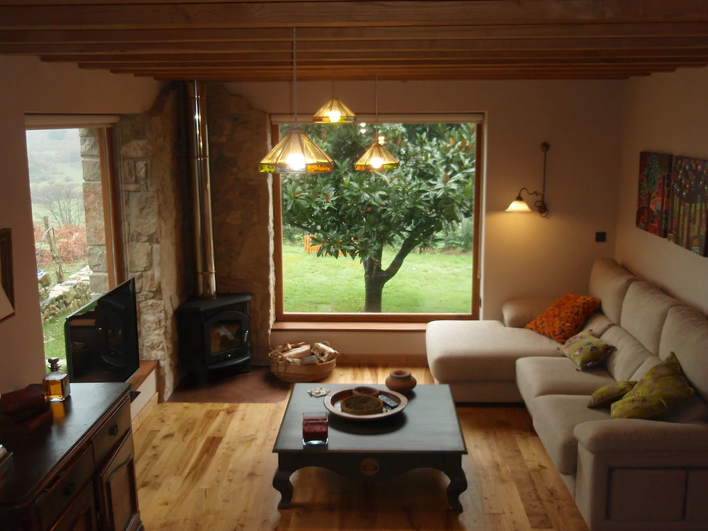 Salón con chimenea, techo con vigas de madera y un ventanal con vistas al jardín.