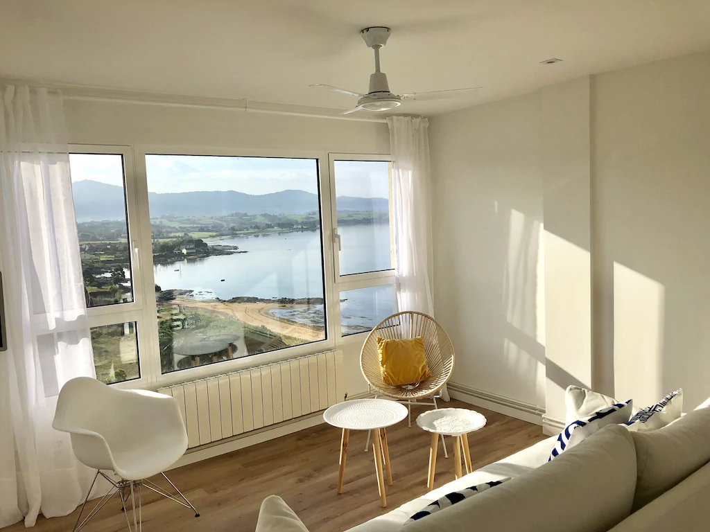 Salón con un sofá, varias sillas y un ventanal con vistas al mar y a las montañas