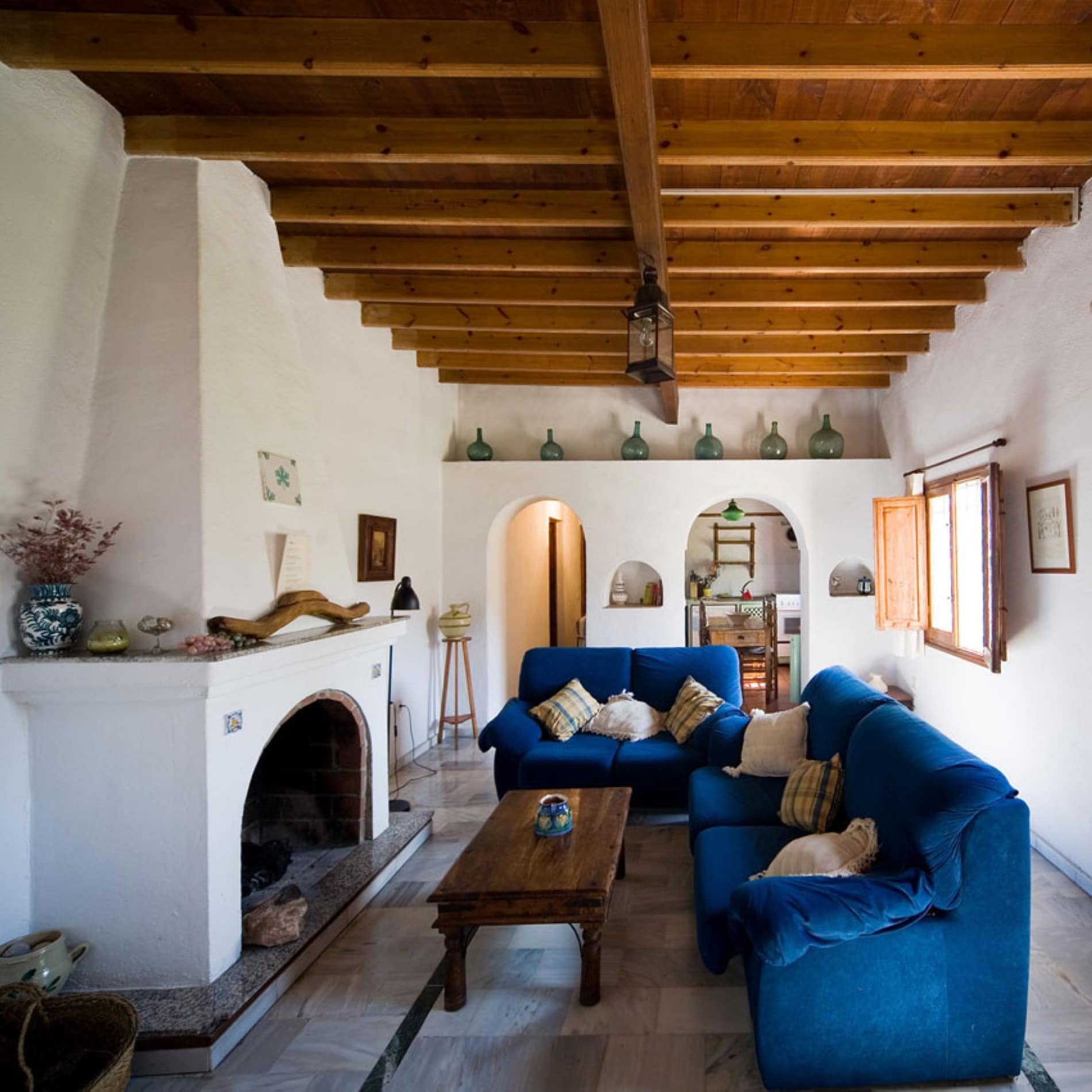 Salón decorado con chimenea y vigas de madera en el techo; iluminación con la luz natural que entra por las ventanas