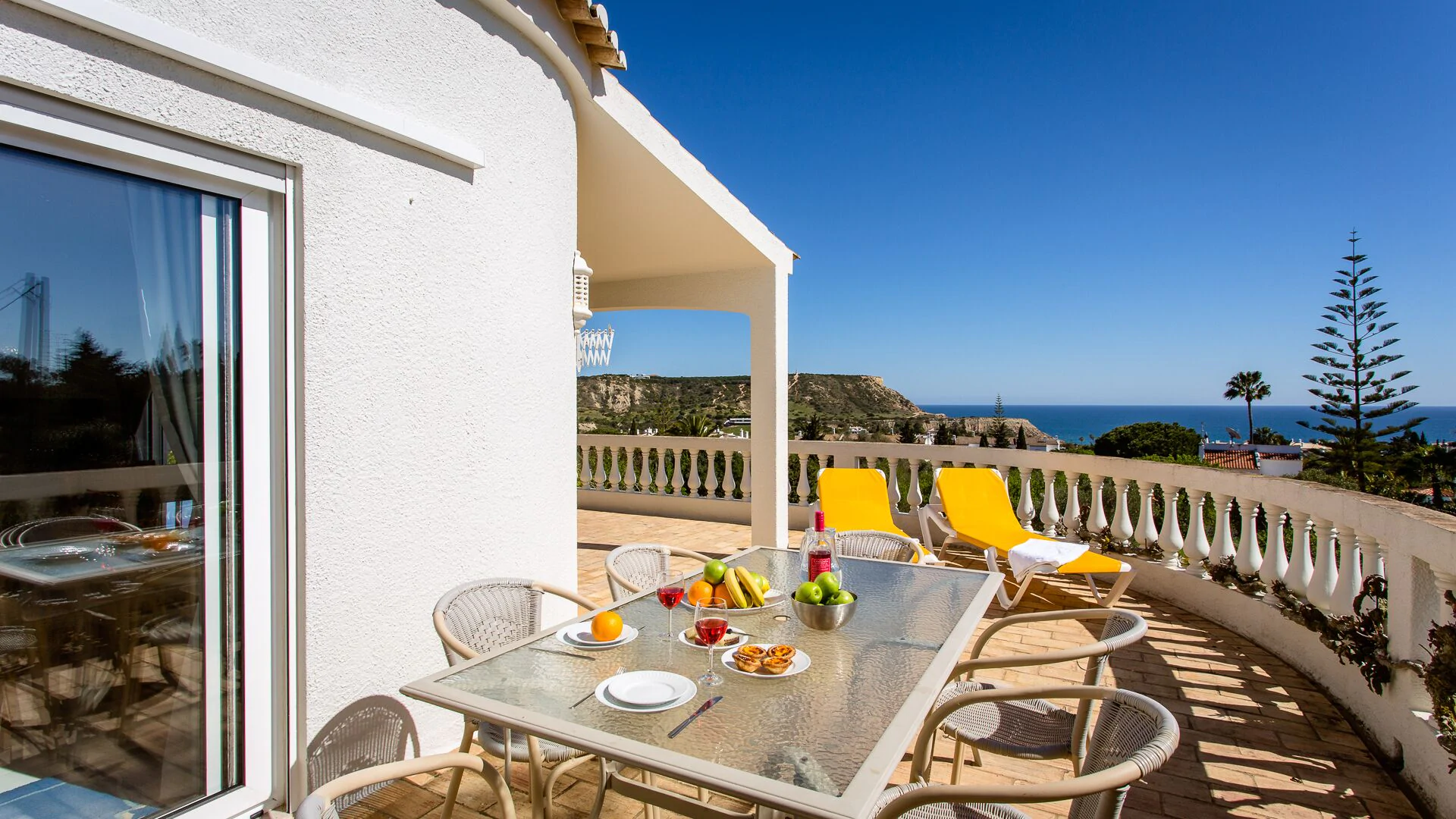Gran terraza con vistas al mar, y una mesa preparada para desayunar y tumbonas