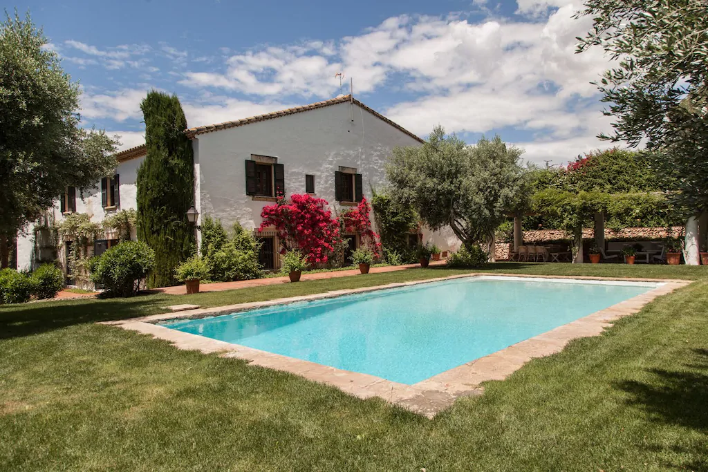 Exterior ajardinado de una finca de dos pisos con amplia piscina