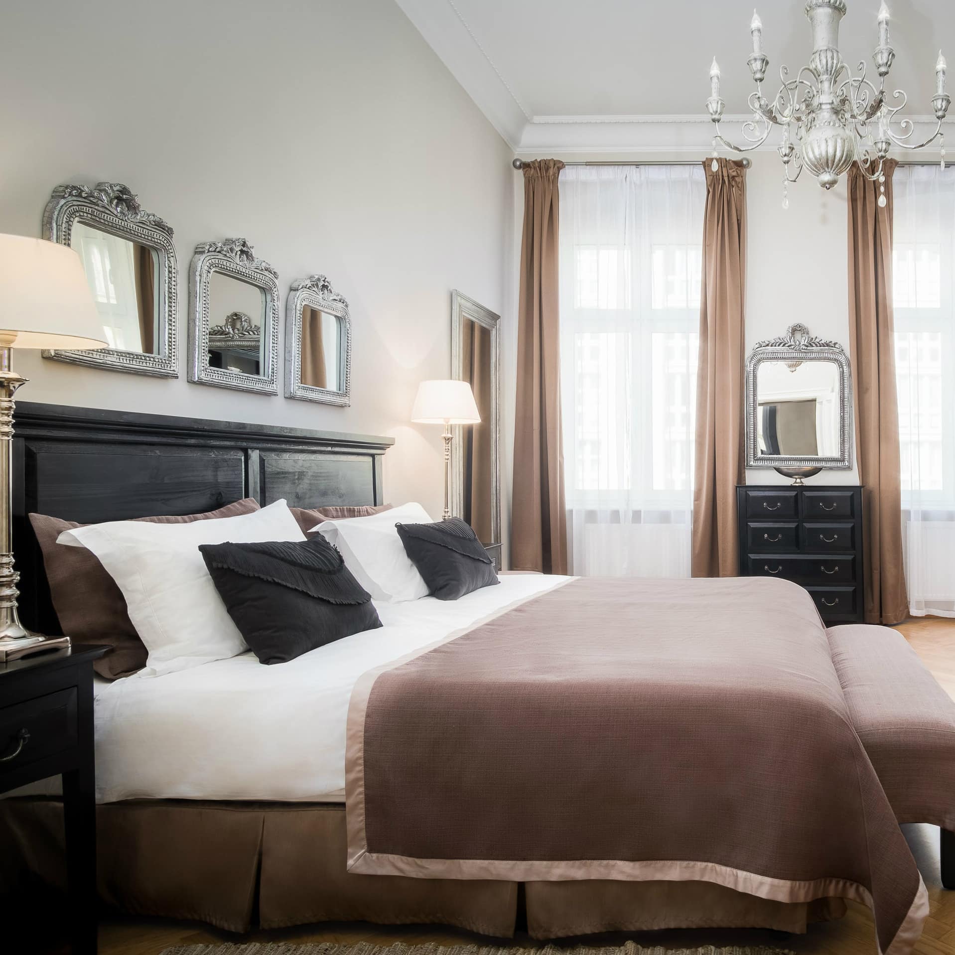 Luxe slaapkamer met elegant bed, hoge ramen, kroonluchter en chique spiegels.